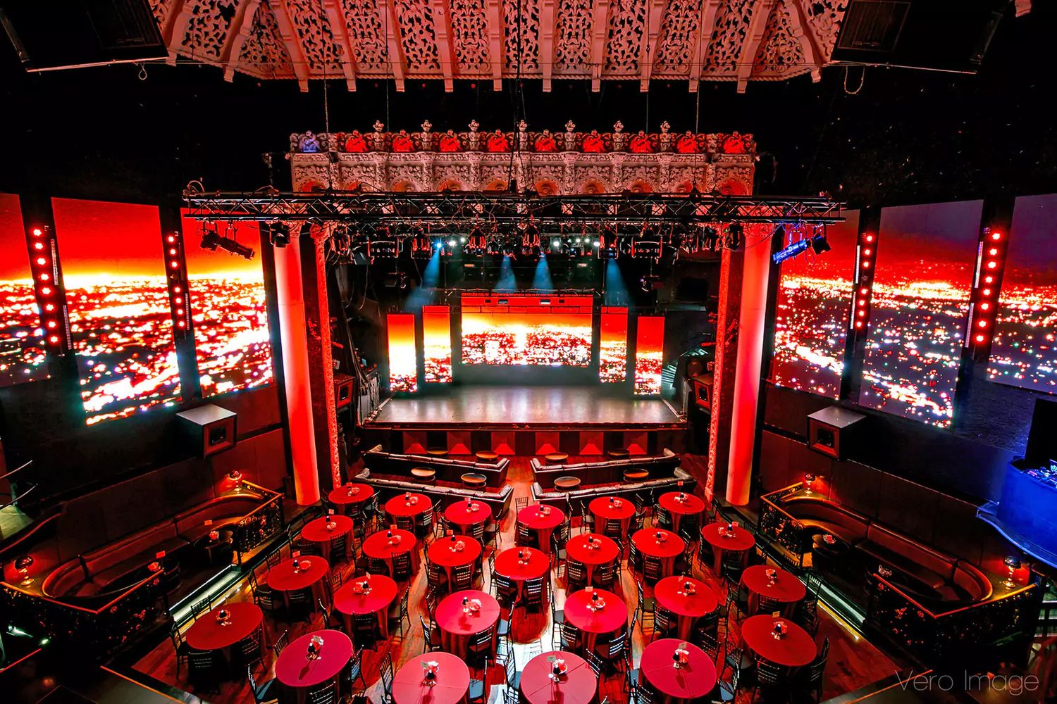 Colorful red and blue stage lighting illuminates an empty concert venue setup with equipment and instruments.
