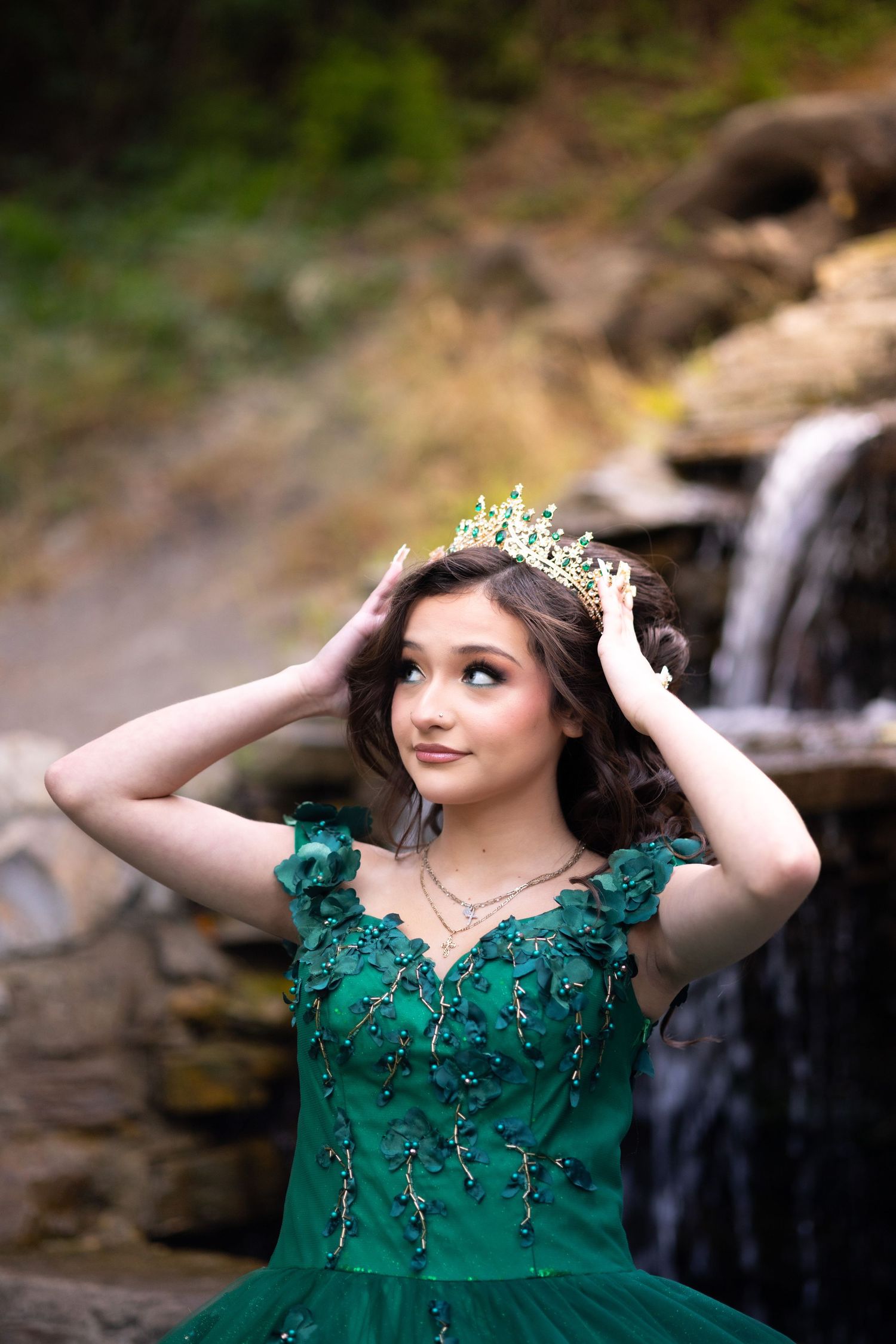 Emerald green formal dress with crystal crown photographed near a cascading waterfall.