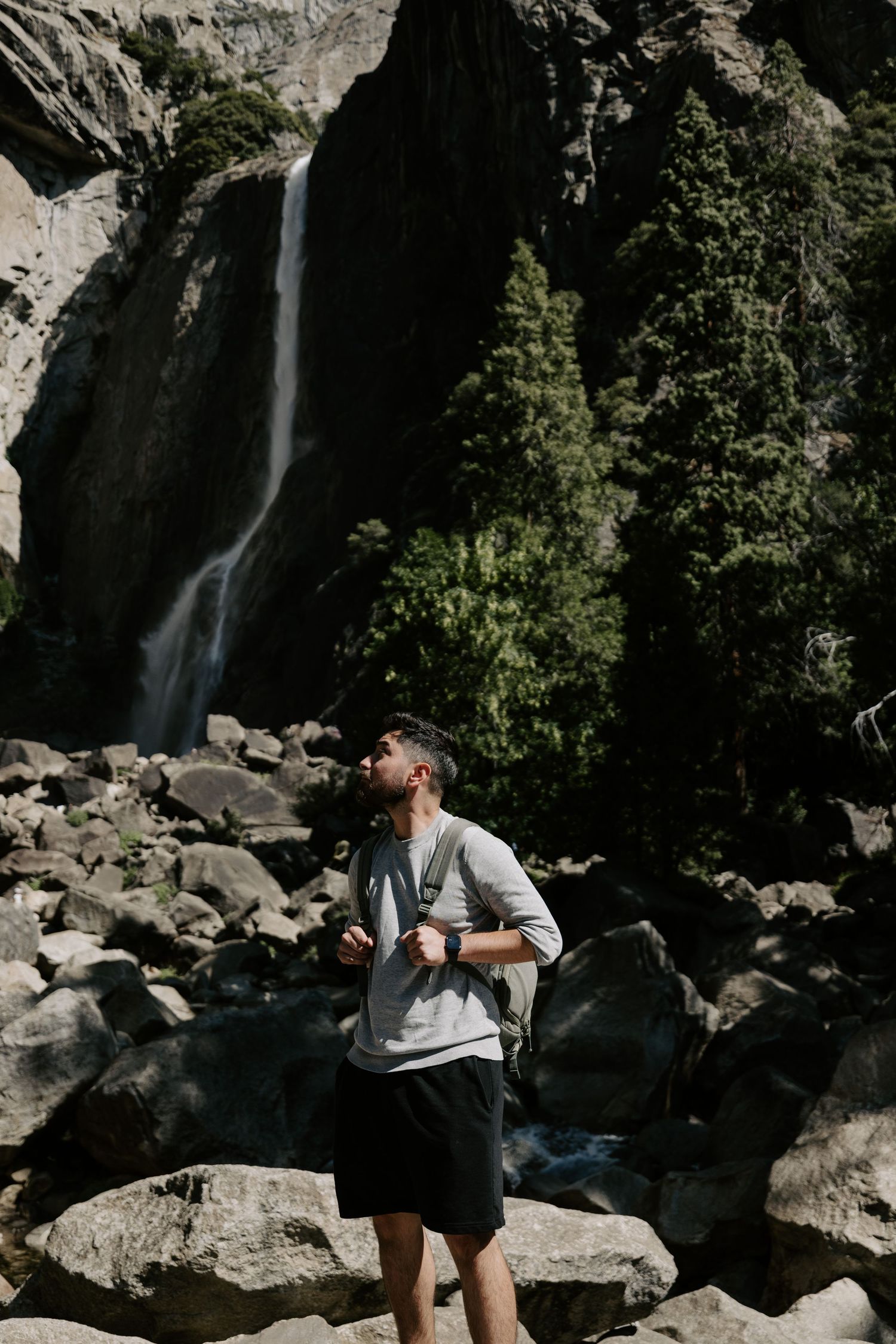 A hiker stands on rocky terrain in front of a dramatic waterfall and cliffs.
