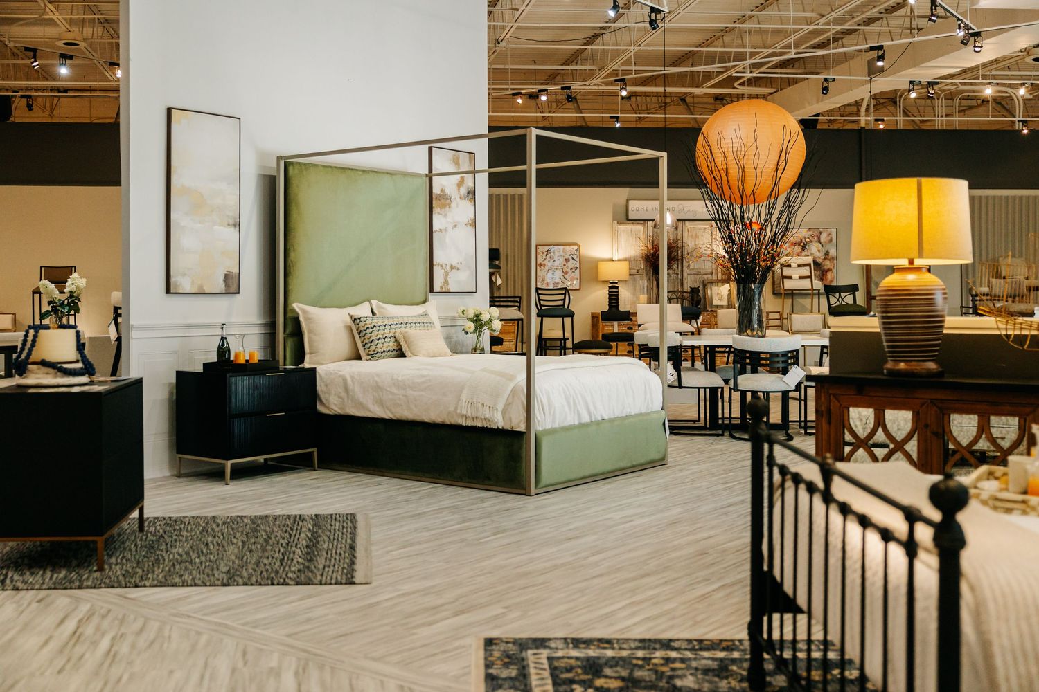 Elegant furniture showroom featuring green upholstered four-poster bed with stylish bedroom decor.