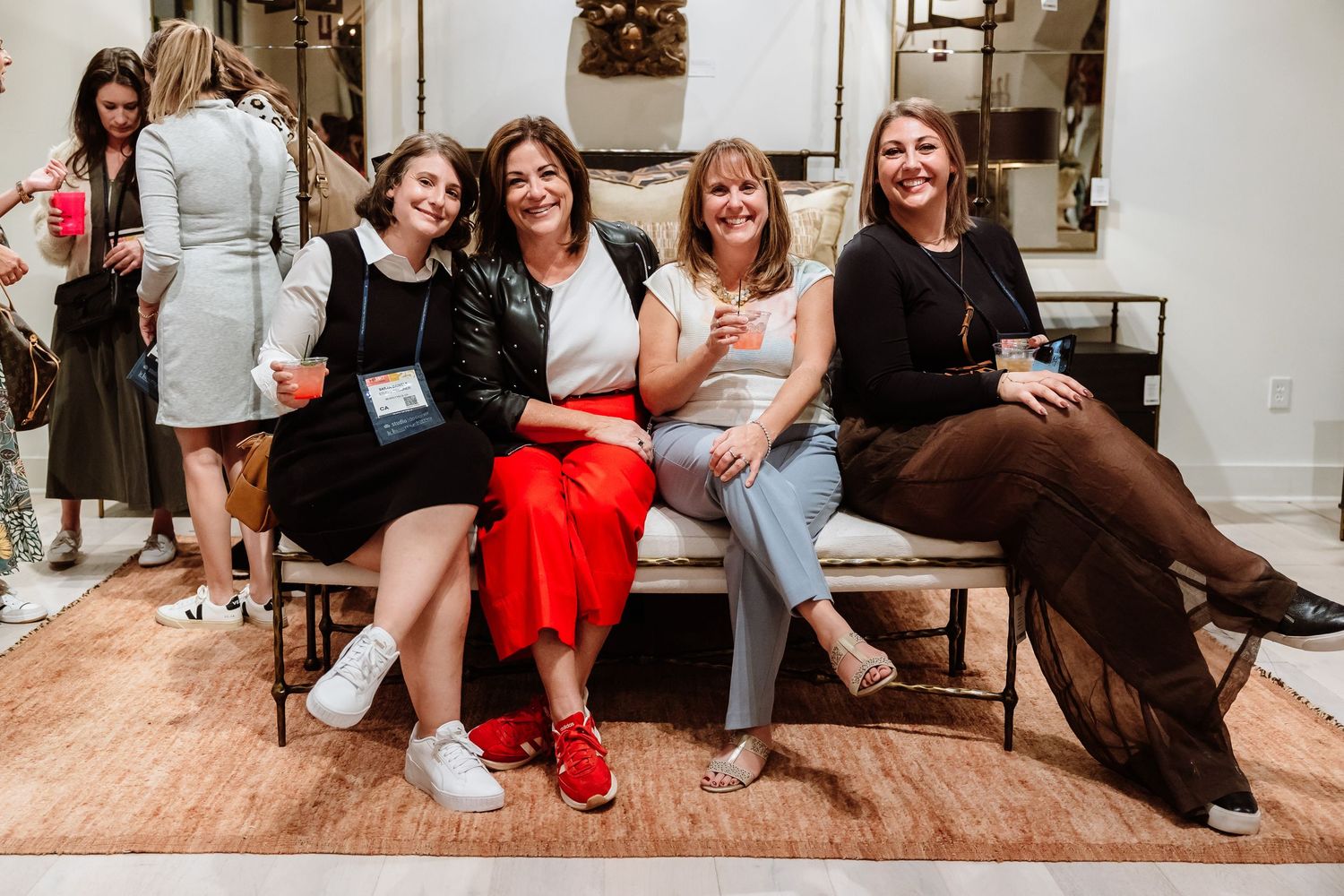 Four women smile and pose together seated on a bench at an interior design showroom event.