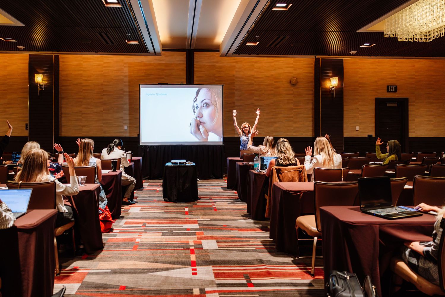 Attendees seated in rows during a conference presentation with a projected image on screen.