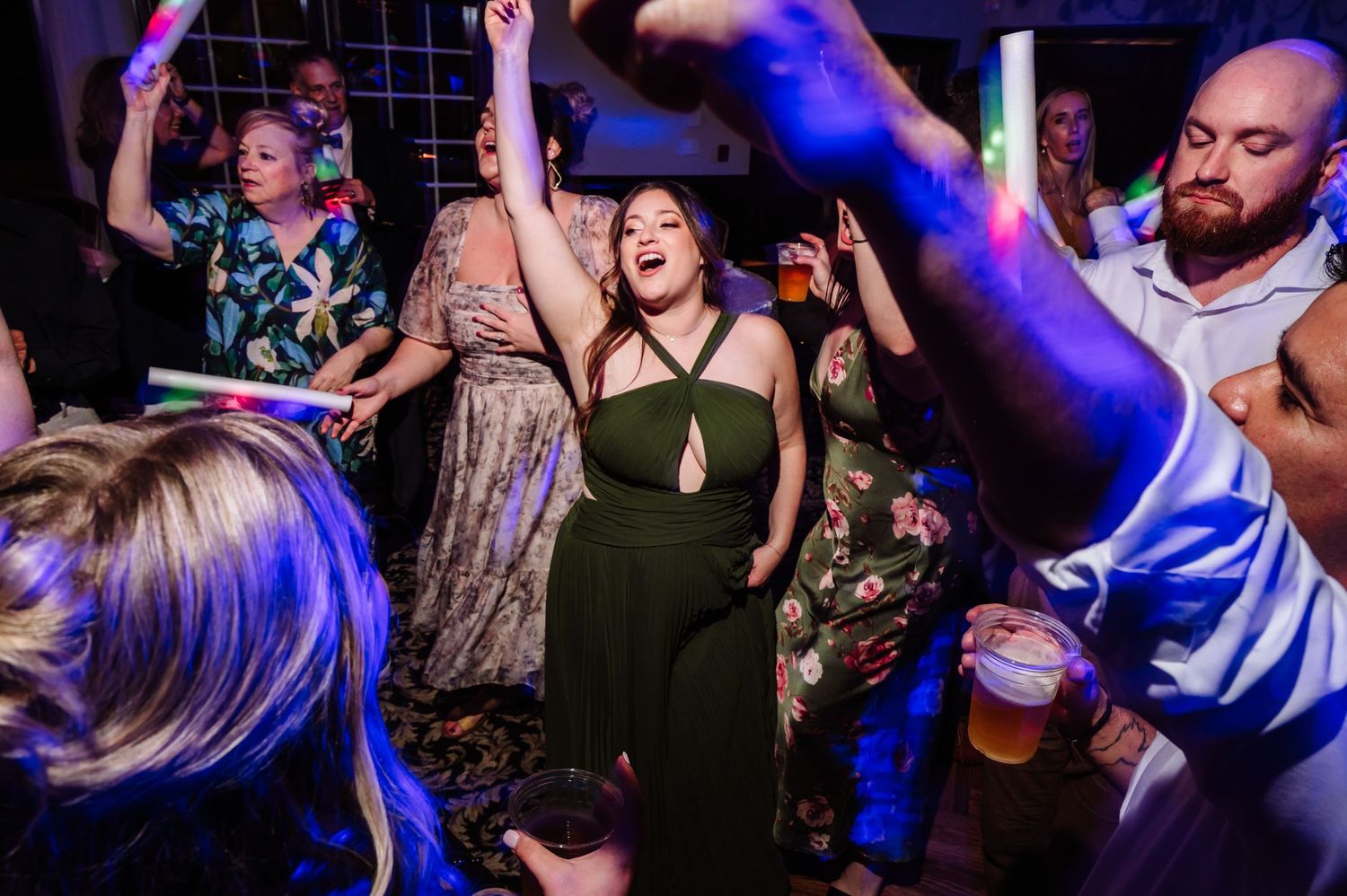 Guests dancing energetically with glow sticks under red lights at a fun late-night wedding party.