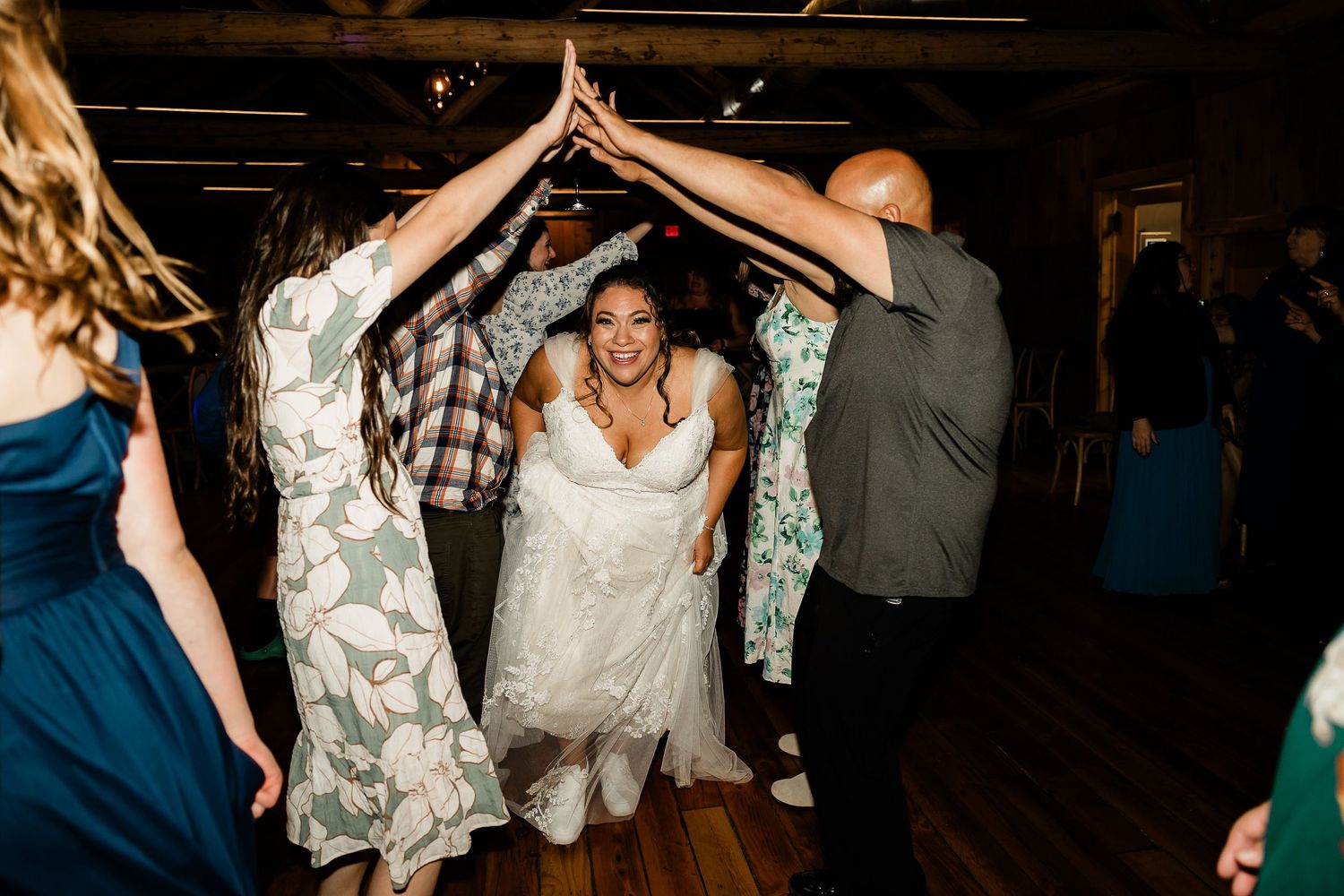 Bride walks through tunnel of raised hands formed by wedding guests on dance floor at reception.
