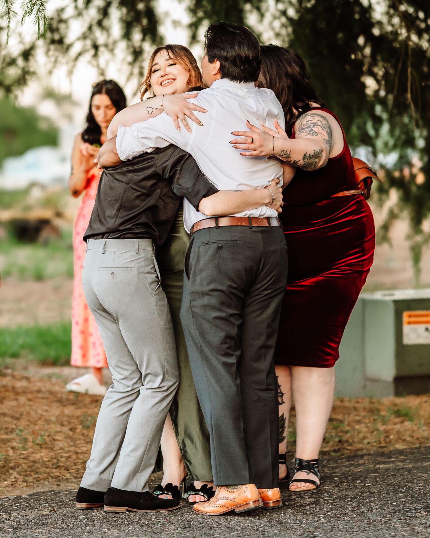 Group of friends sharing a warm group hug outdoors at a wedding celebration.