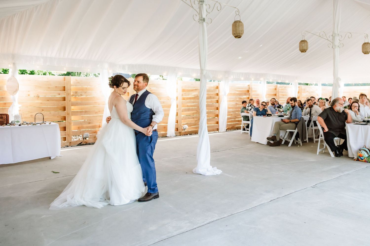 Bride and groom share their first dance under an elegant white tent at their wedding reception.