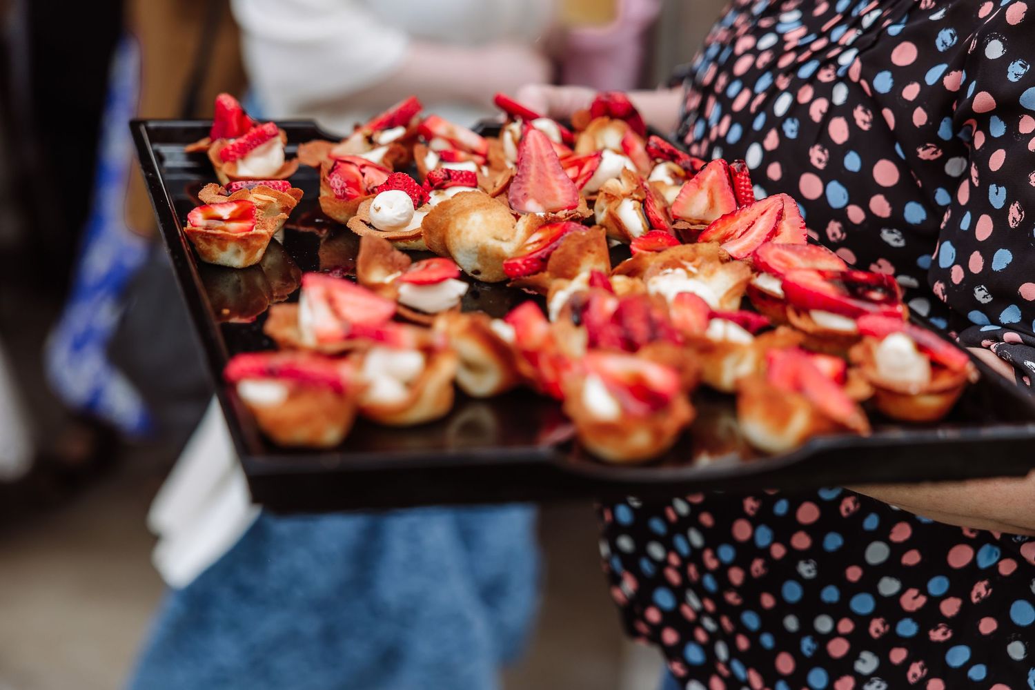 Server holding tray of elegant red and white appetizers at wedding reception.