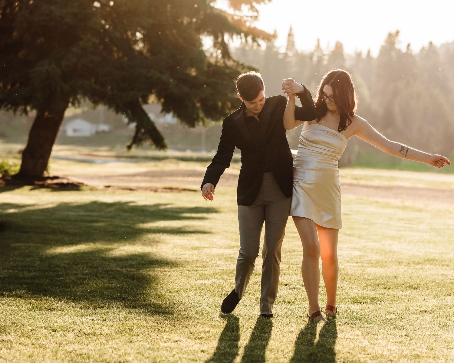Couple dances joyfully on a sunlit green lawn with warm golden light all around them.
