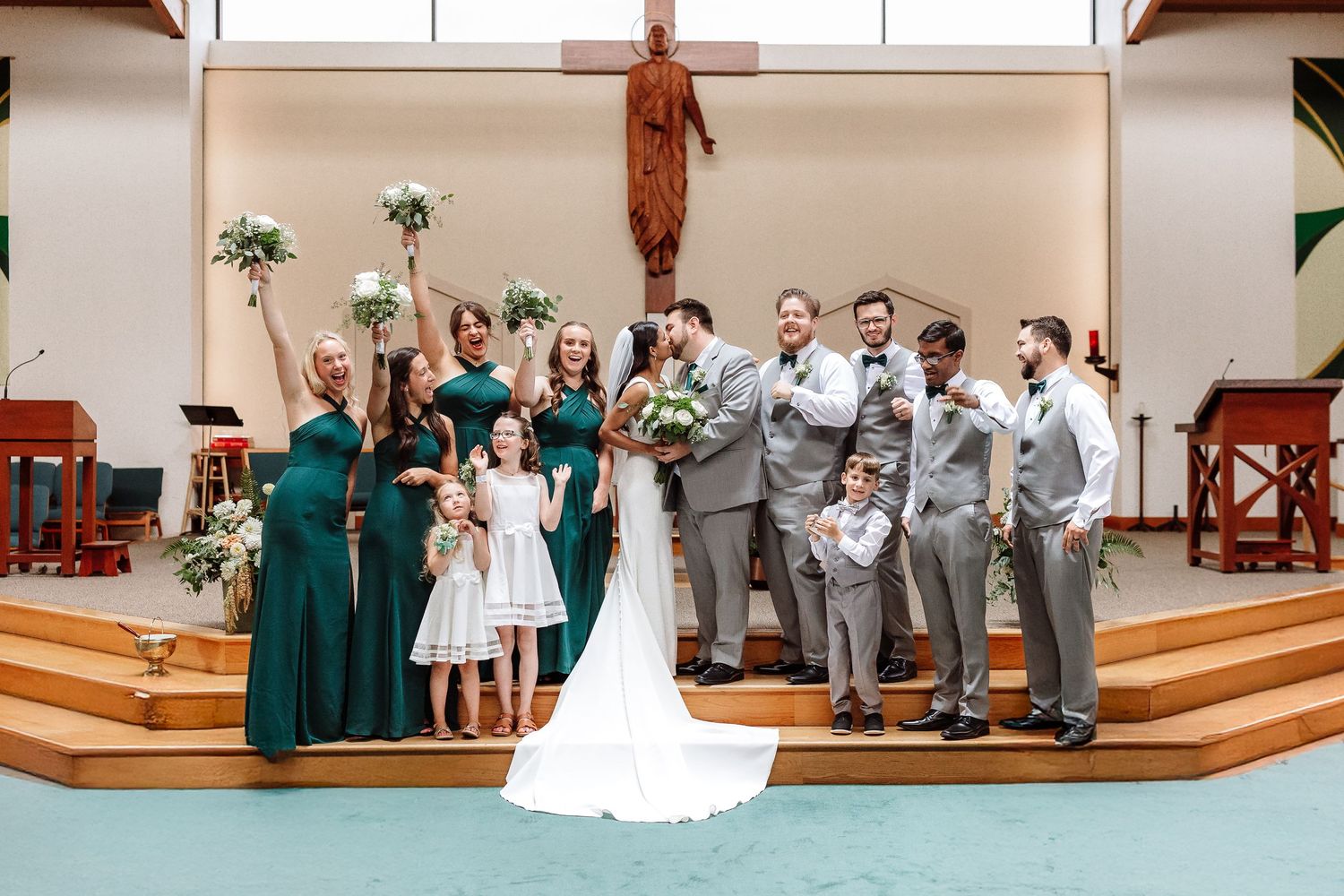 A wedding party celebrates at a church altar with bridesmaids in green and groomsmen in gray suits.