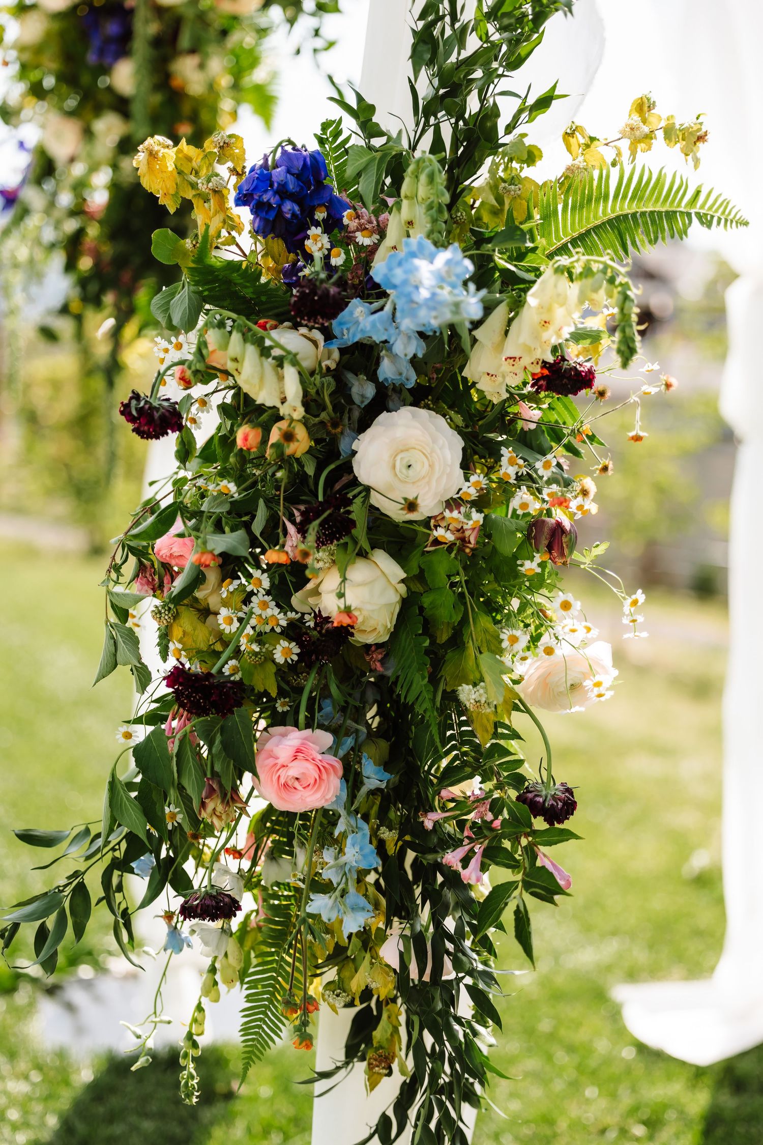 Lush floral arrangement with blue, white, pink, and yellow blooms on a white wedding ceremony arch.