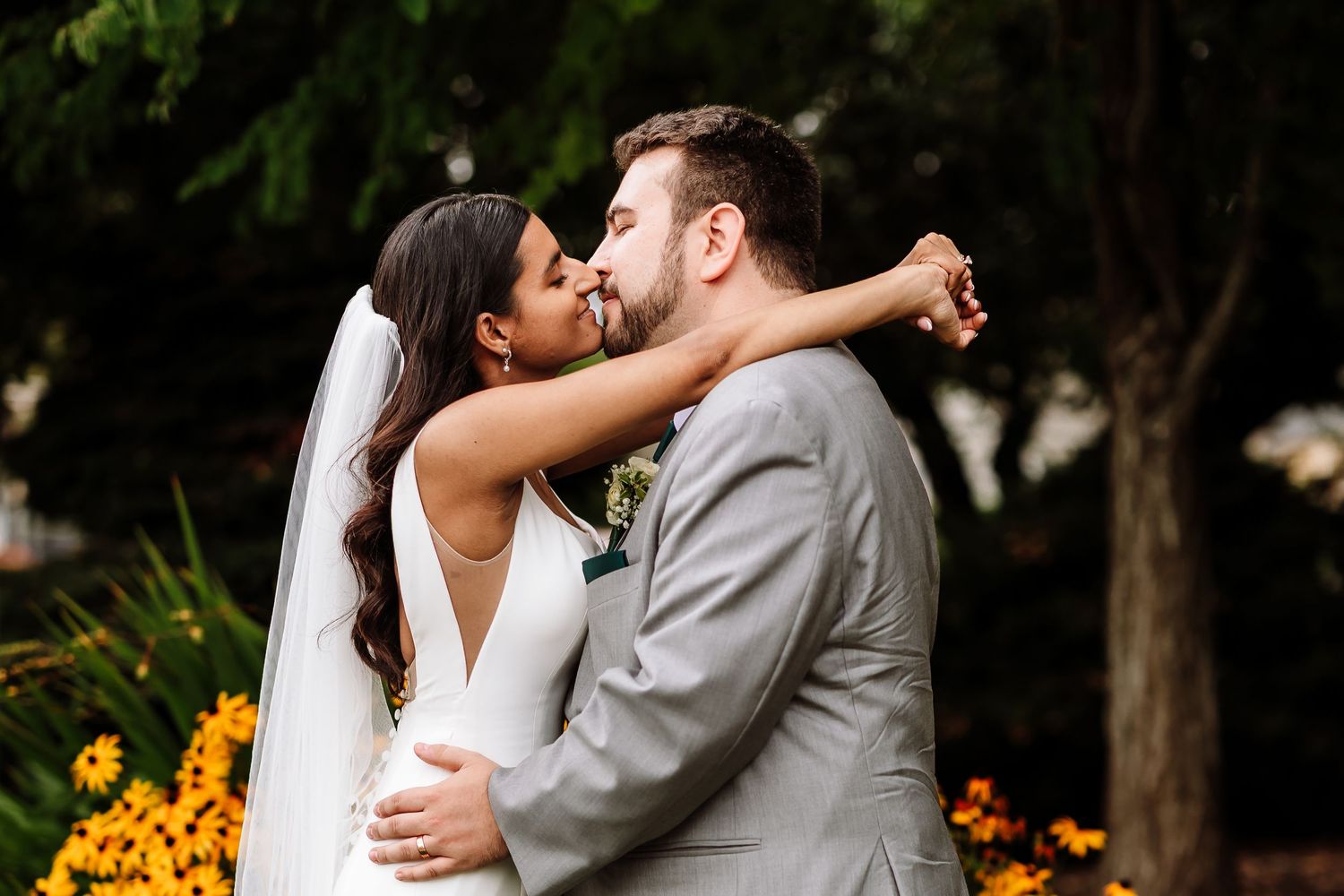 Bride and groom sharing a romantic almost-kiss moment surrounded by vibrant yellow flowers.