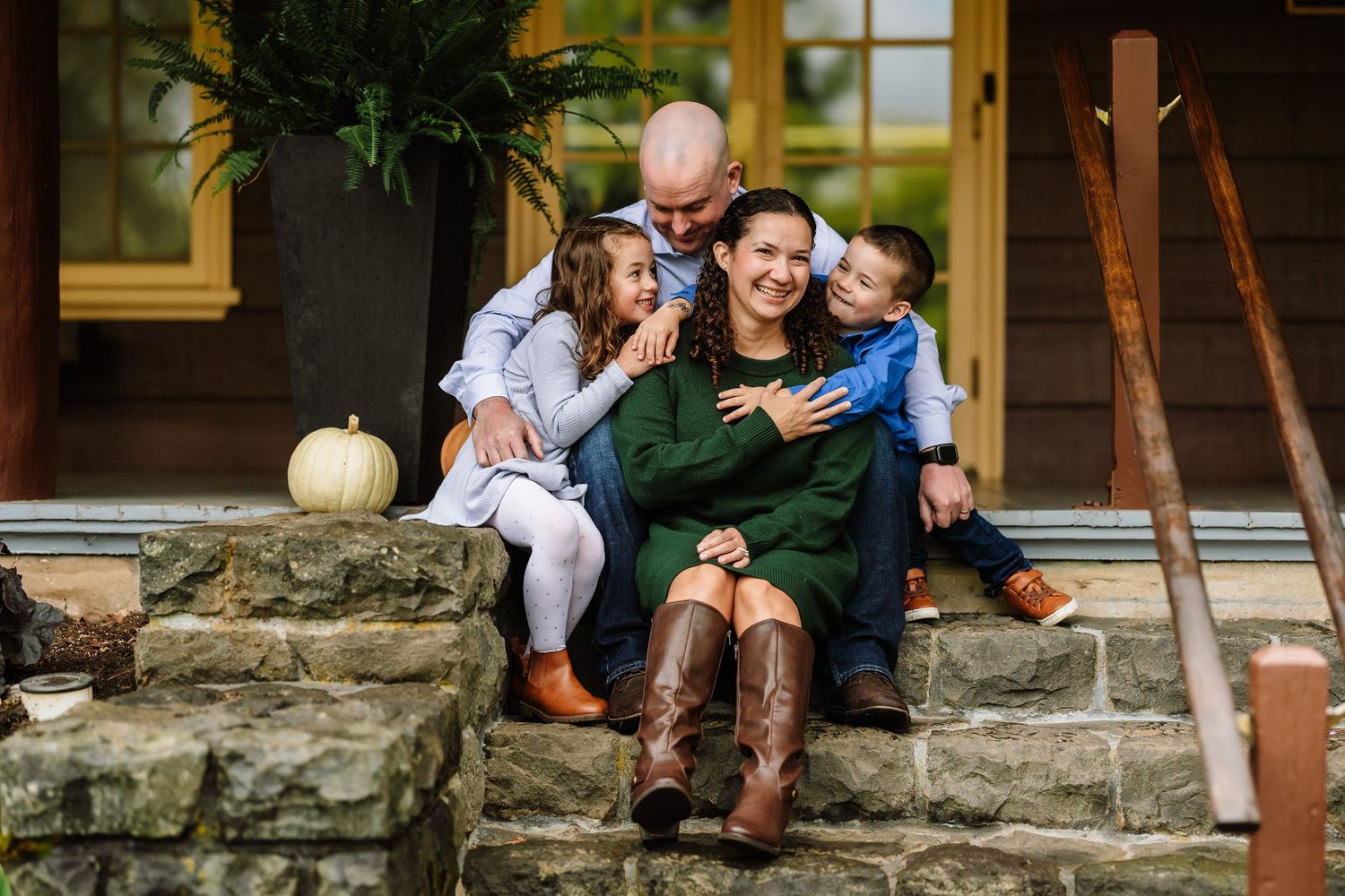 Happy family of four posing on stone steps of a rustic home porch in autumn, smiling and embracing warmly.
