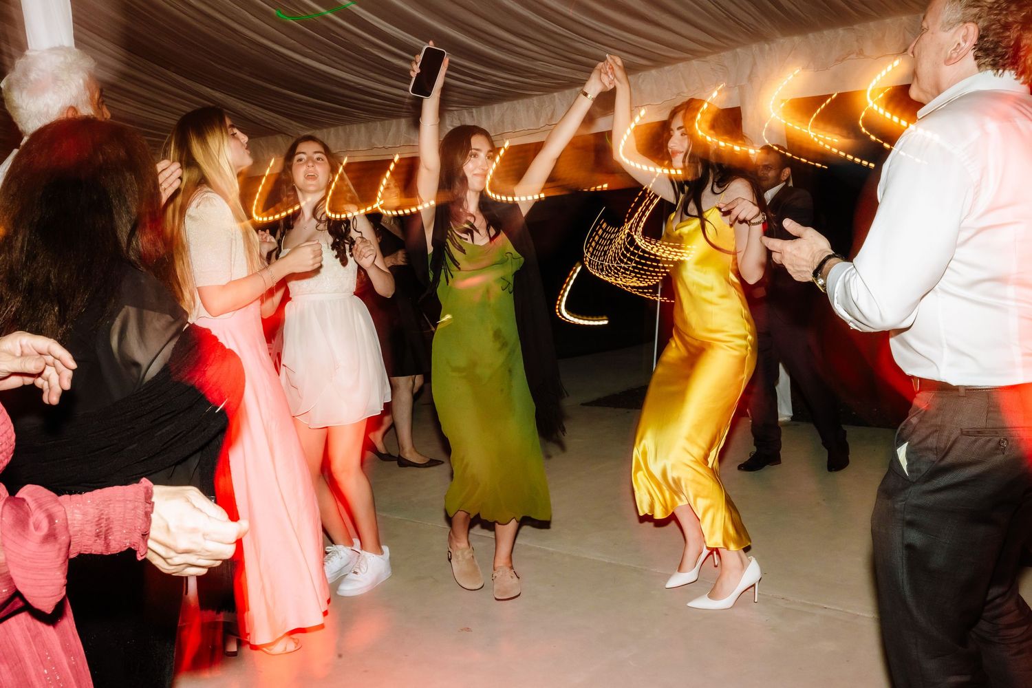 Guests dancing energetically under festive lights at a lively wedding reception celebration.