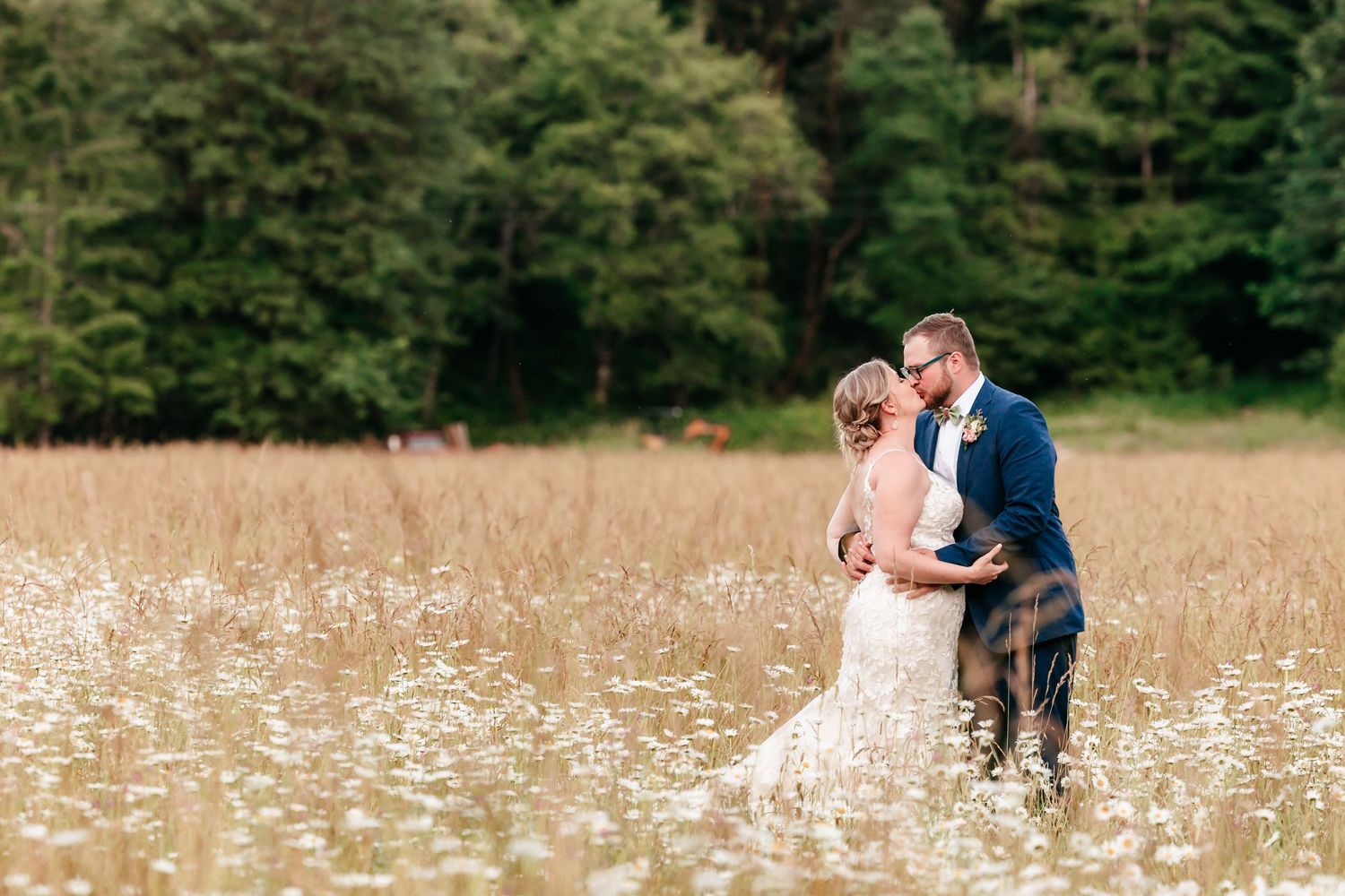 Bride and groom sharing a romantic kiss in a field of wildflowers with a lush green forest backdrop.