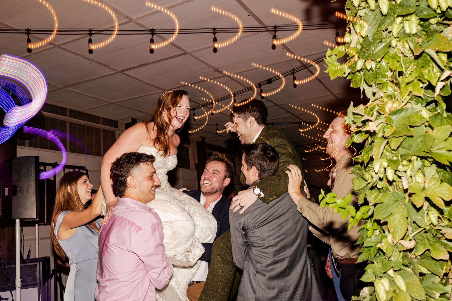 Wedding guests lift the bride and groom in celebration on a festively decorated dance floor.