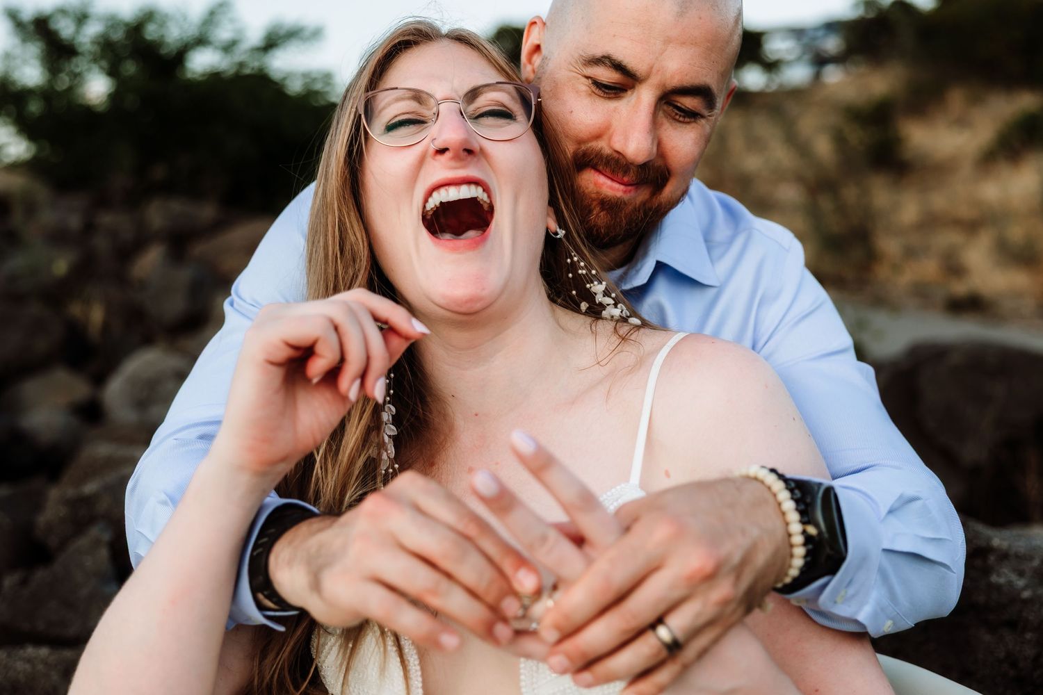 Laughing woman with glasses and man with beard share a joyful embrace during outdoor engagement photos.