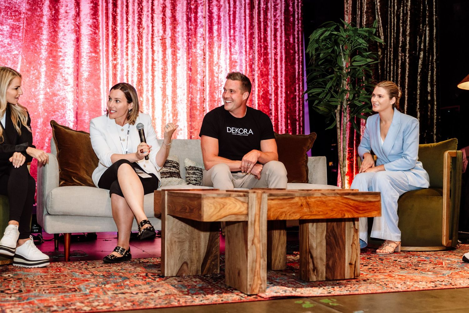 Four professionals seated on stage during panel discussion at modern conference event with pink backdrop.