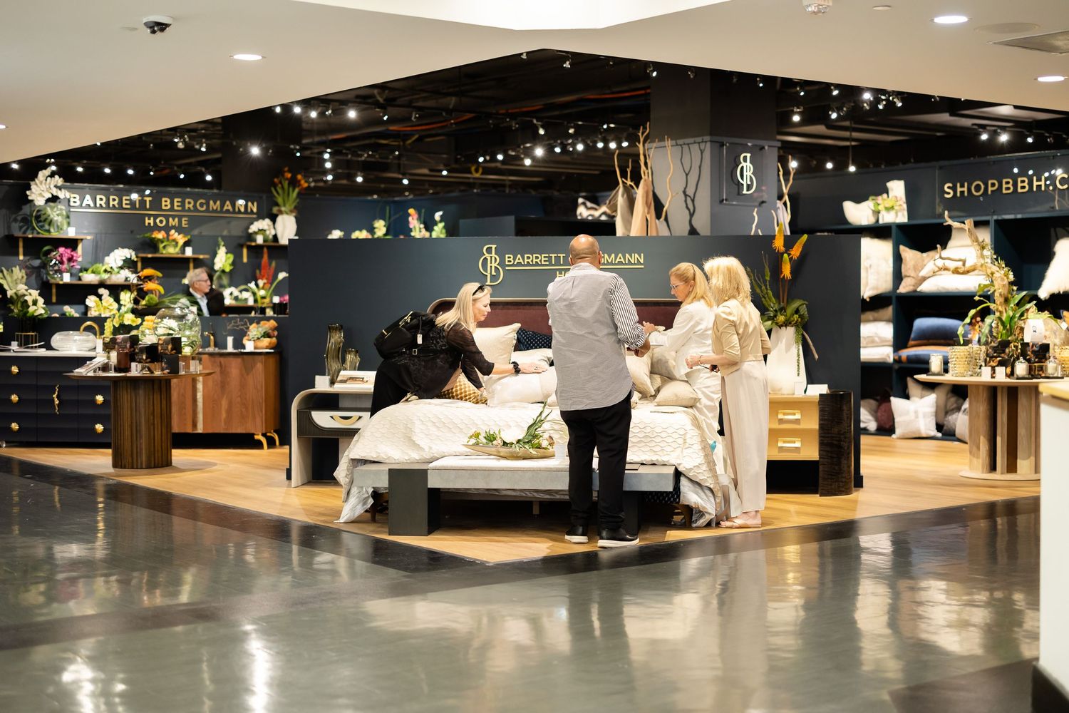 Elegant Barrett Bergmann Home dark showroom display with gold accents and shoppers browsing bedding.