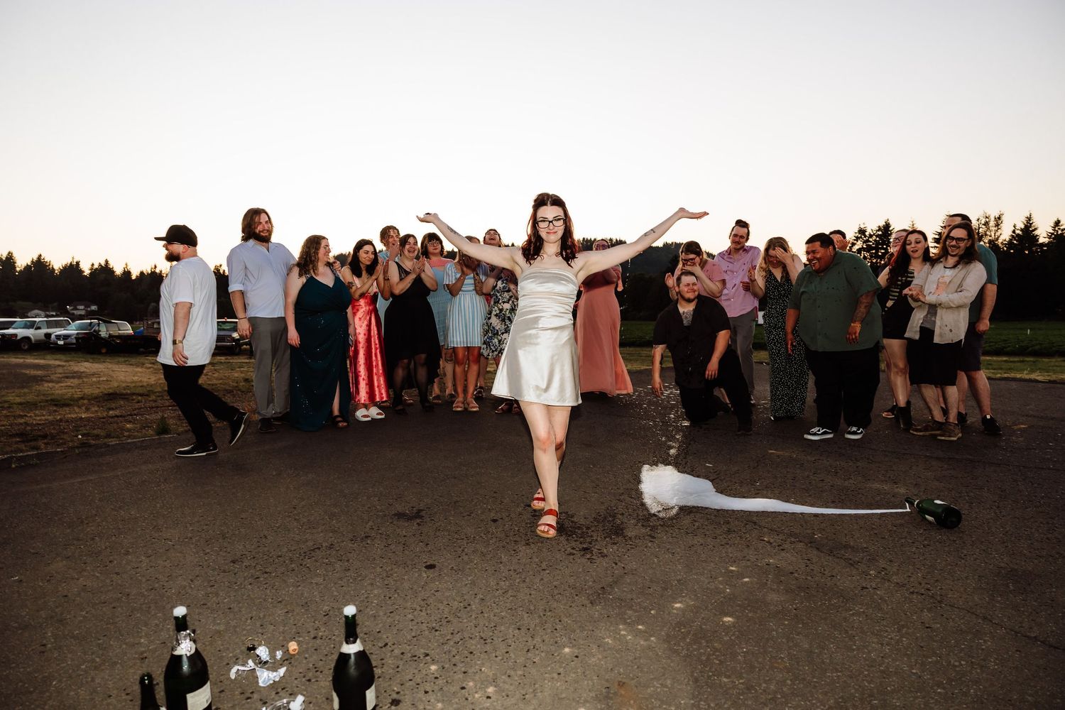 Bride in silver dress dancing outdoors with wedding guests gathered behind her.