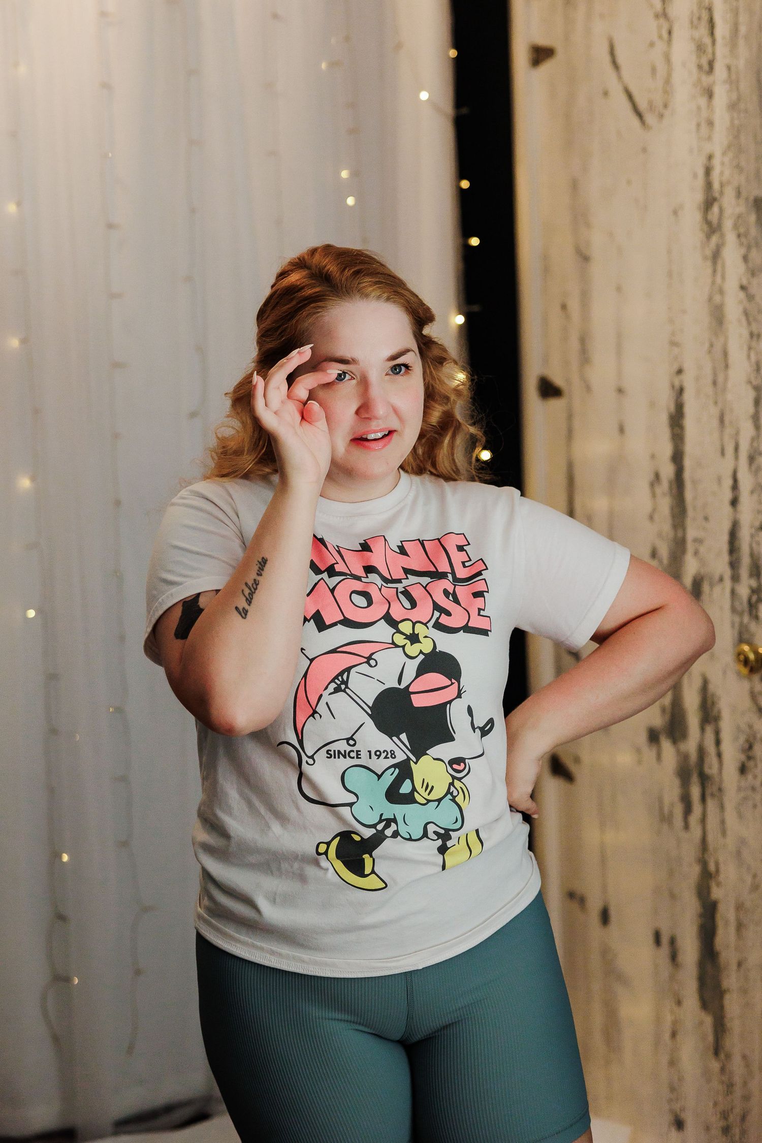 Young woman in a Minnie Mouse graphic tee posing playfully in front of fairy lights.