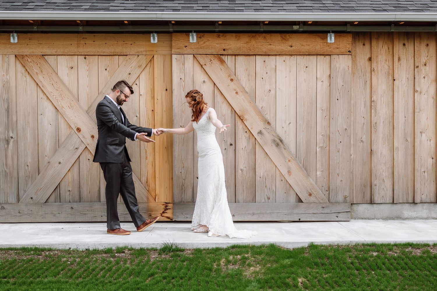 Bride and groom hold hands facing each other in front of rustic wooden barn doors.