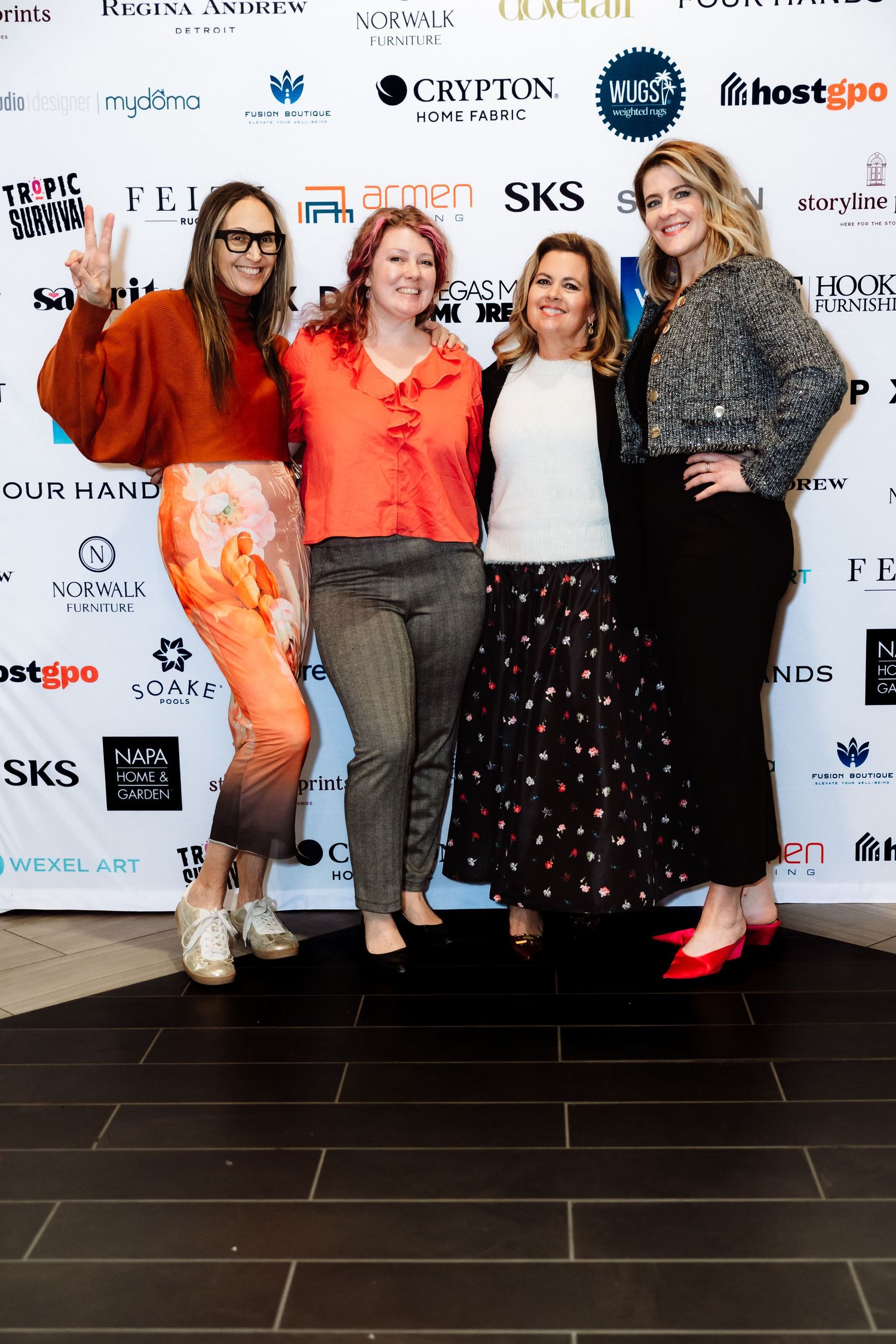 Four women pose together in front of sponsor logos at a design industry event.