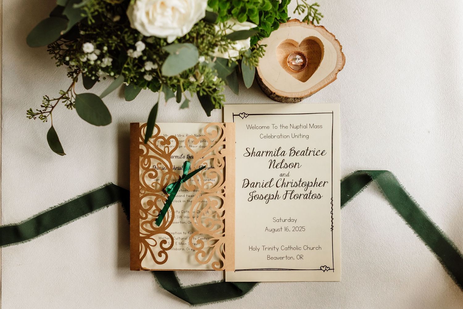 Elegant wedding invitation with laser-cut wooden cover, green ribbon, floral bouquet, and gold rings on a white background.
