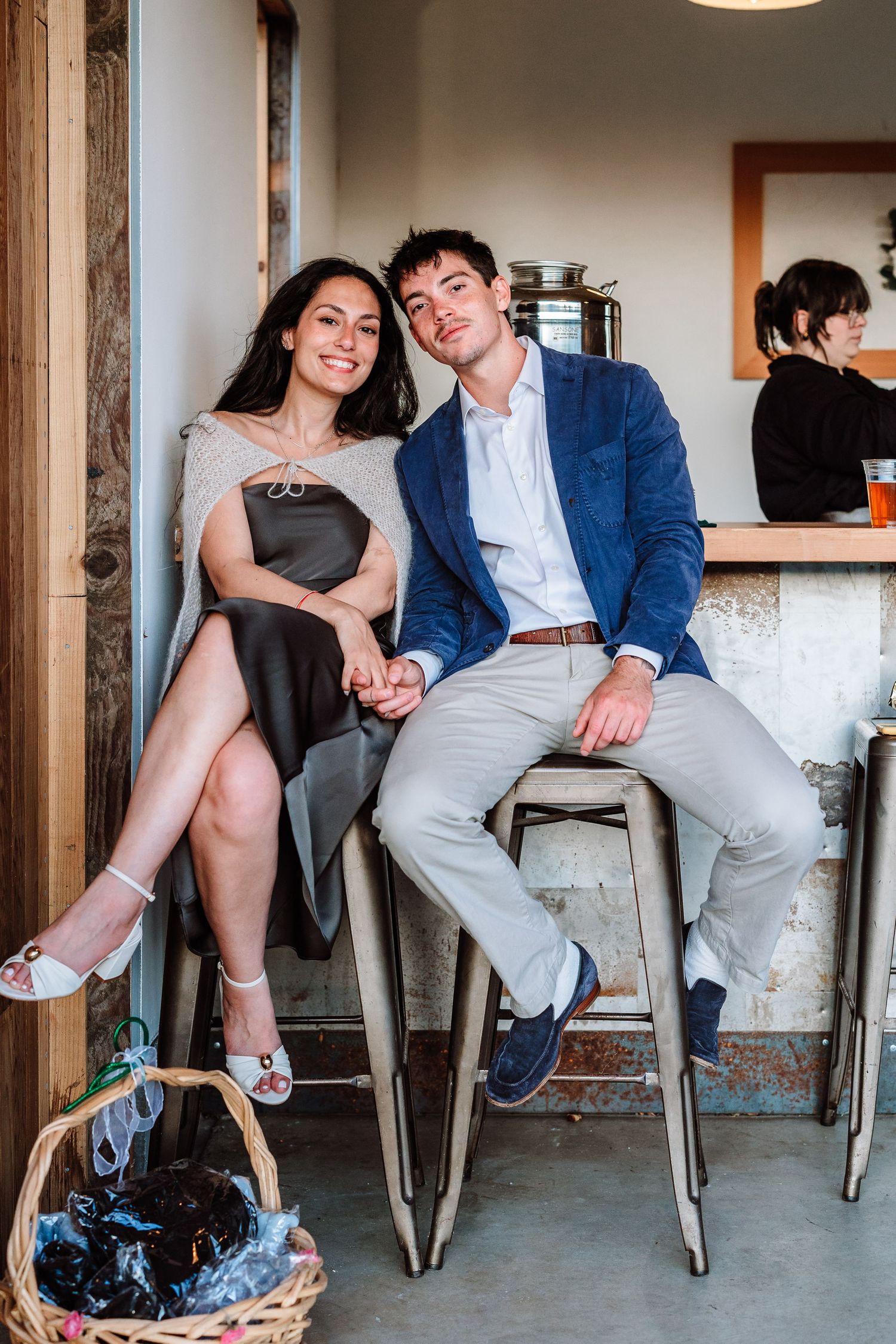 Smiling couple sitting together on bar stools holding hands at a casual wedding venue.