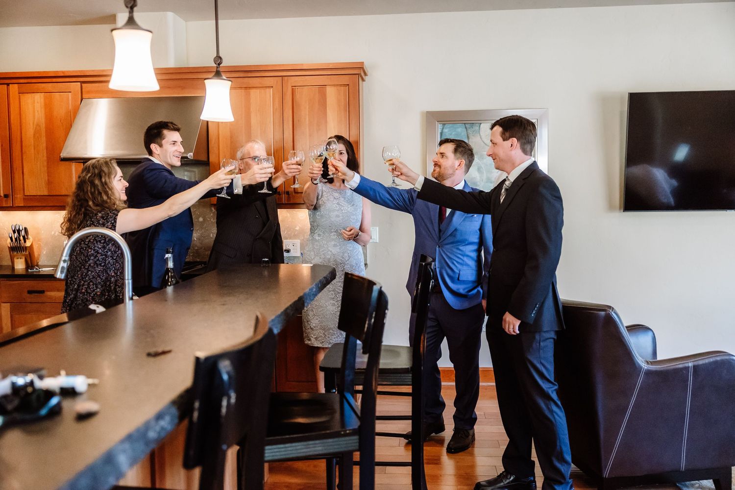 Wedding party raises glasses in a toast around a kitchen island before the ceremony.