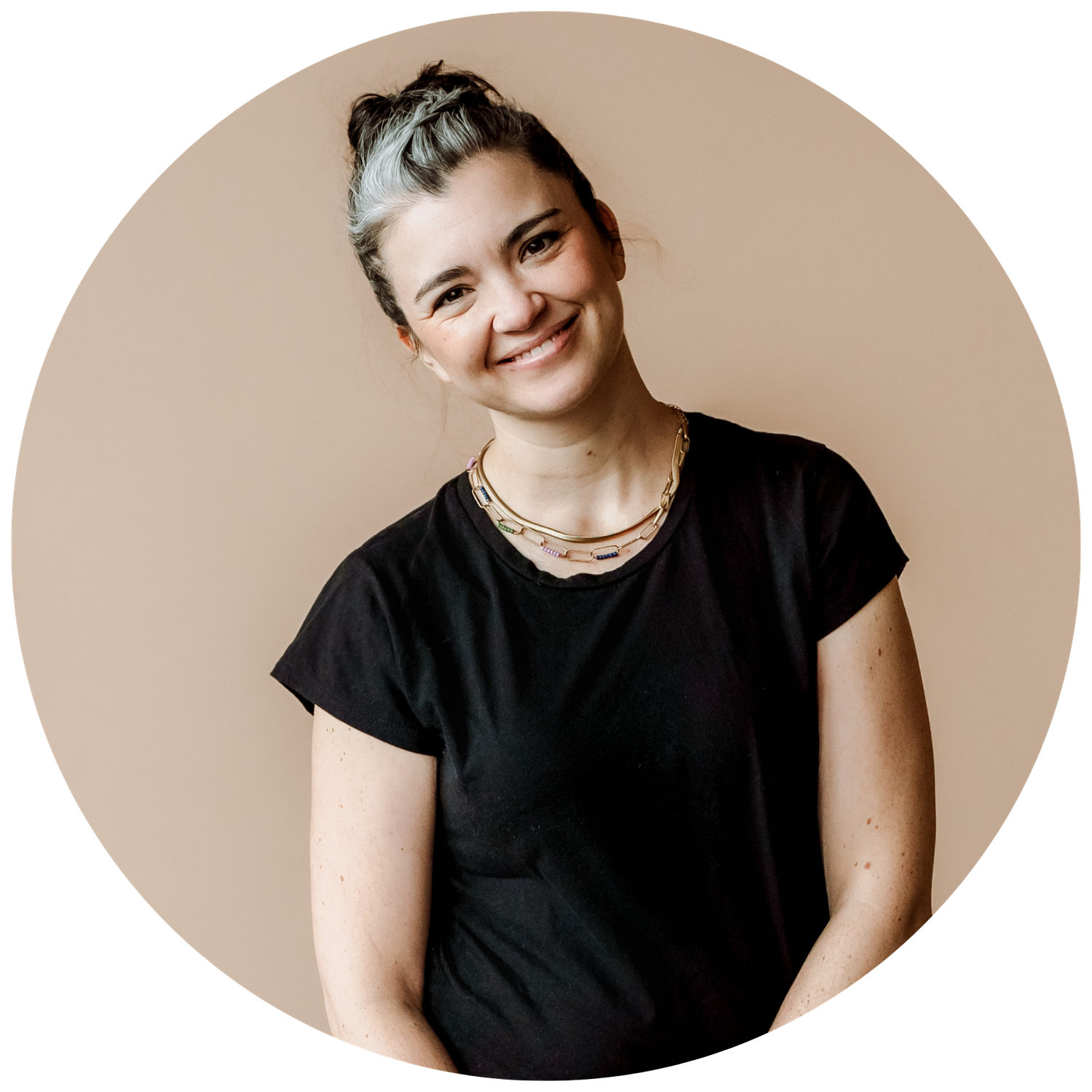 A circular portrait of a smiling woman with gray hair wearing a black t-shirt and gold necklace.