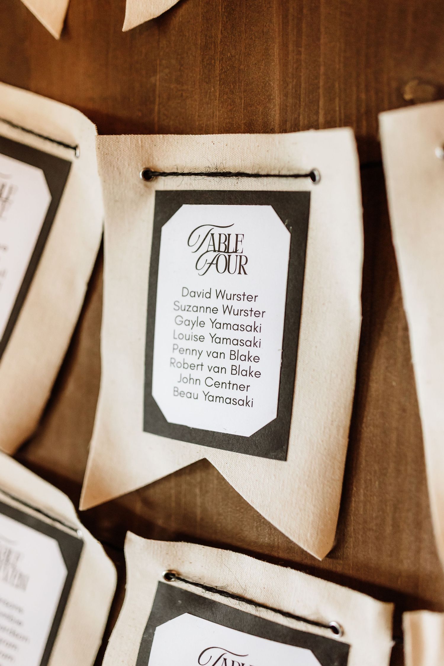 Elegant fabric pennant seating chart cards displaying Table Four guest names on wooden surface.