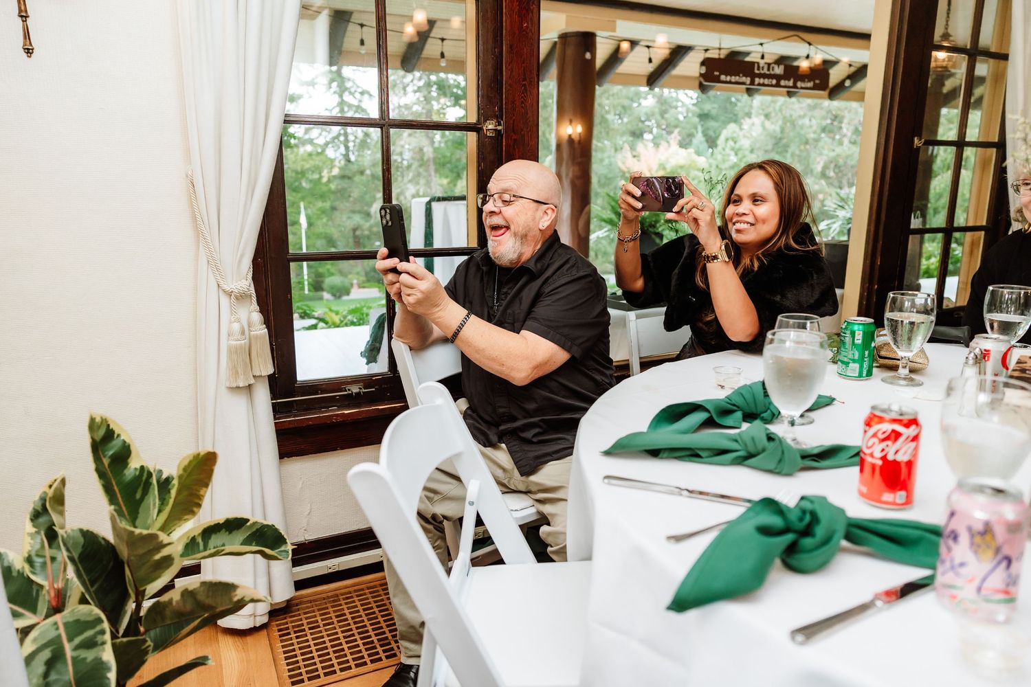 Wedding guests photograph speeches at elegantly decorated reception table with green napkins.