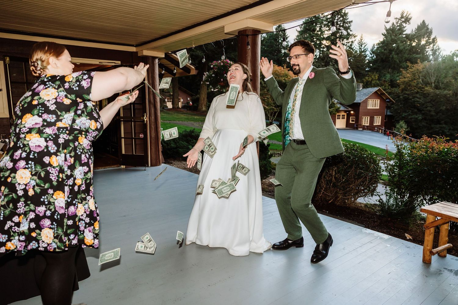 Bride and groom celebrating joyfully as money is tossed in the air on a covered porch.