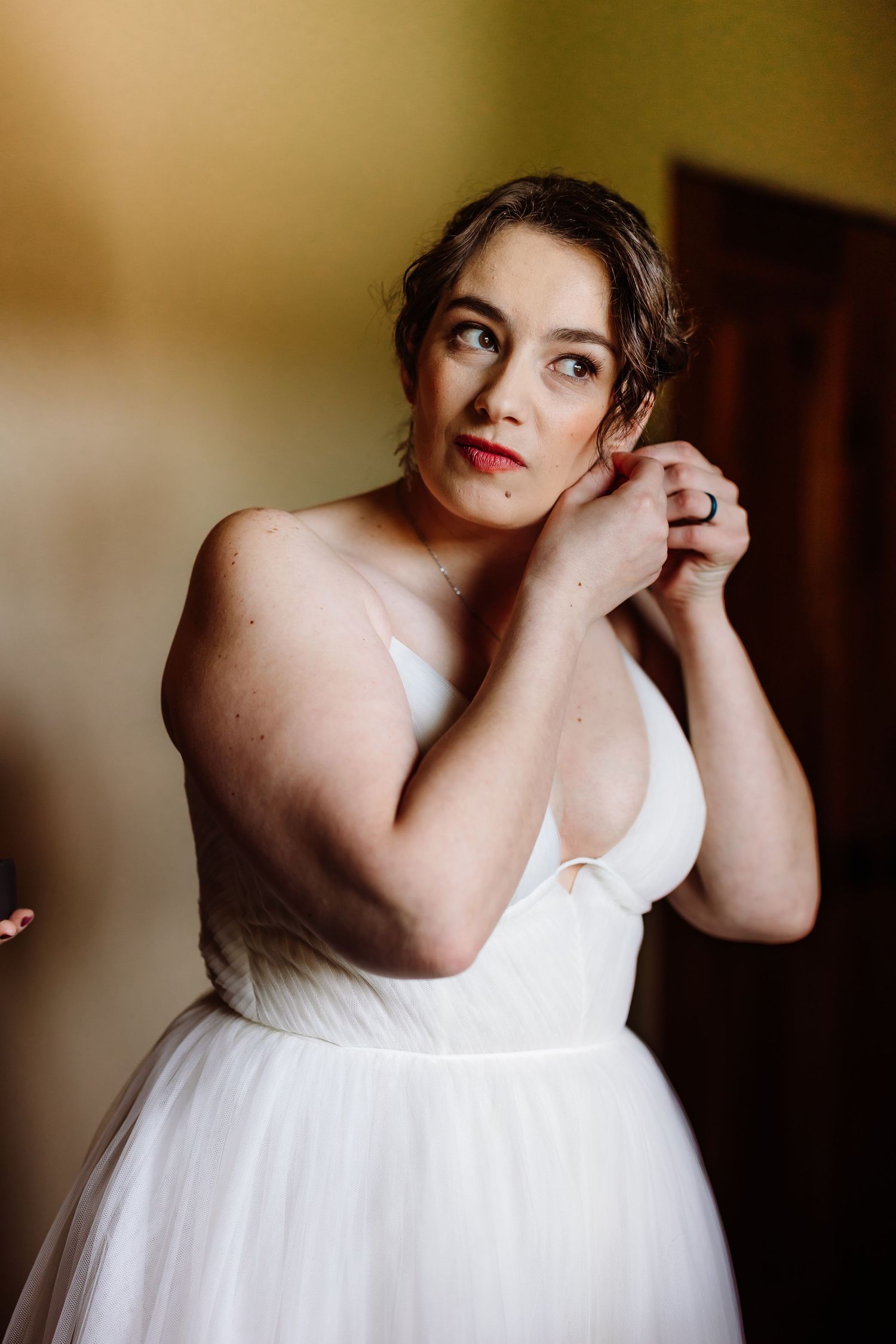Bride in strapless white tulle gown puts on earrings while getting ready for her wedding.
