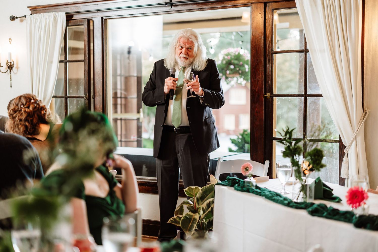 Elderly man with white hair gives wedding toast in elegant wood-paneled reception venue.
