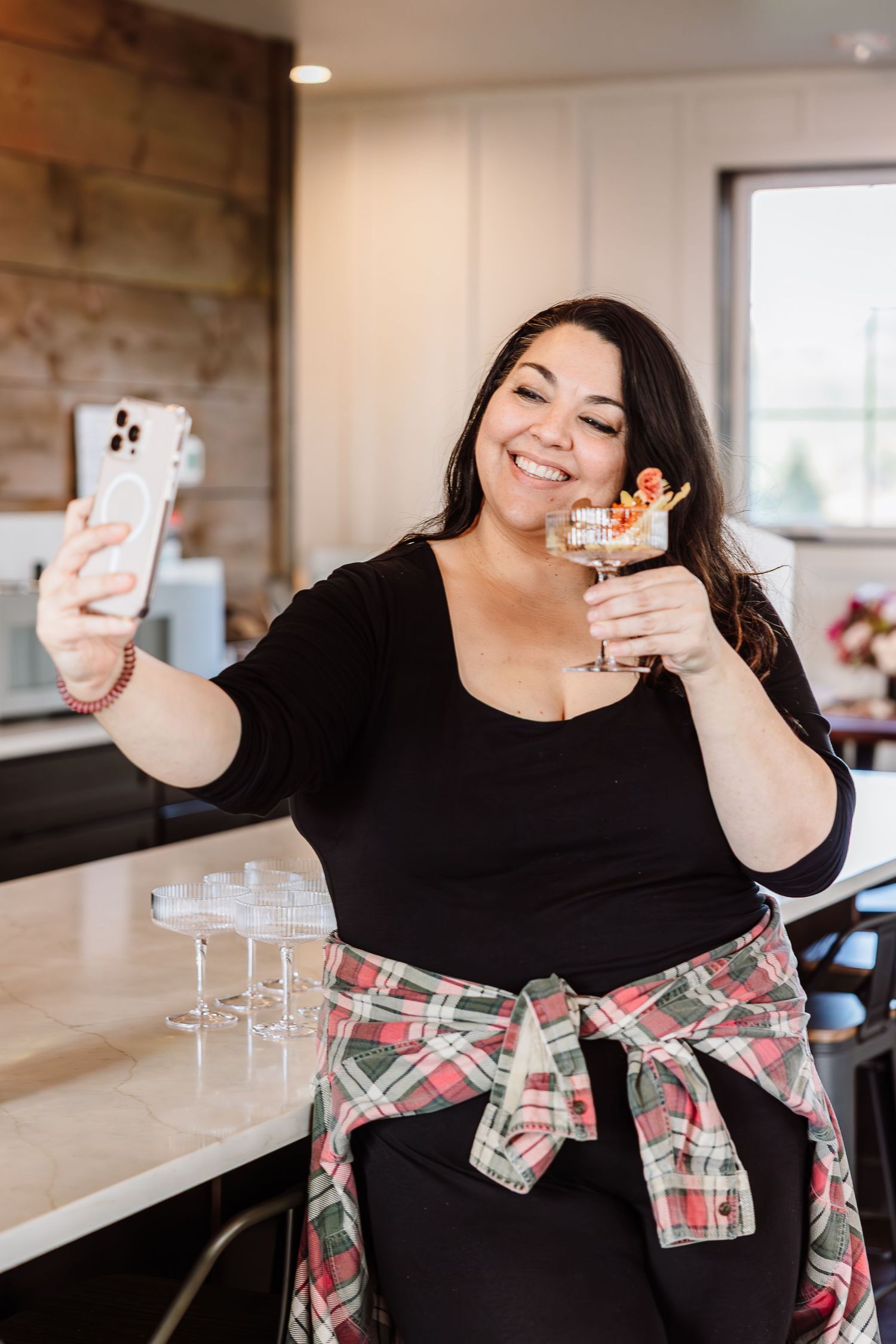 Woman taking selfie with cocktail garnished dessert drink at kitchen counter.
