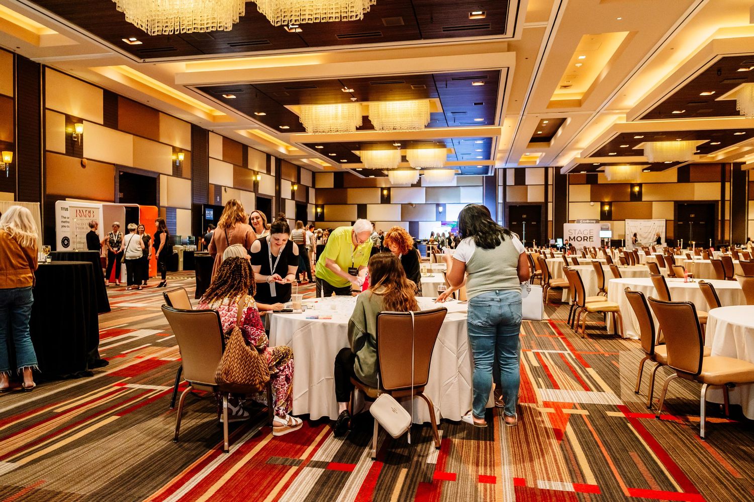 Attendees mingling at round tables in a spacious hotel conference ballroom during a business event.