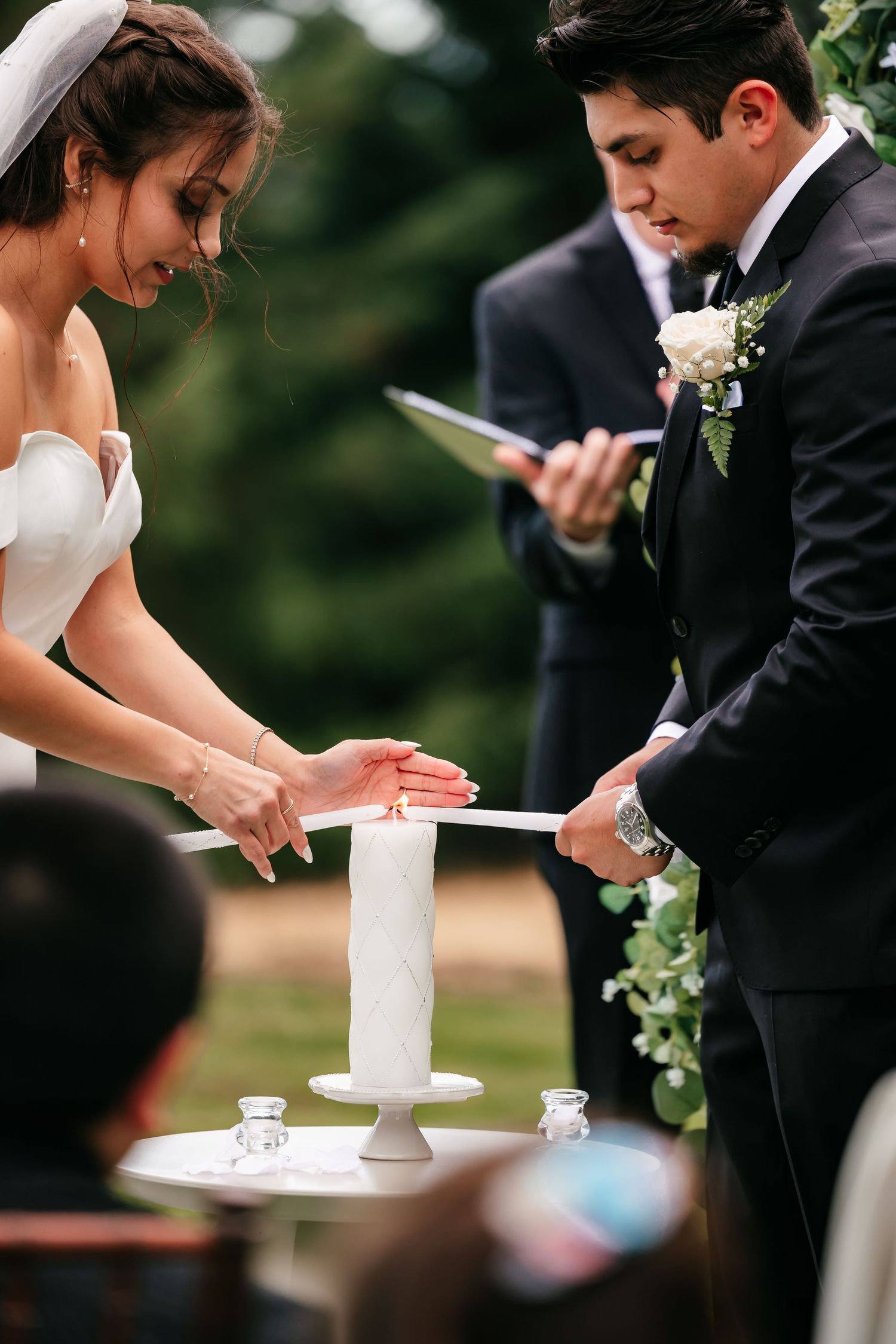 Bride and groom light unity candle together during outdoor wedding ceremony officiated by minister.