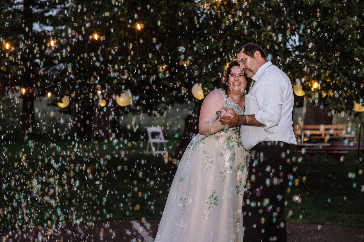 Newlyweds share romantic first dance surrounded by colorful confetti and string lights at dusk.