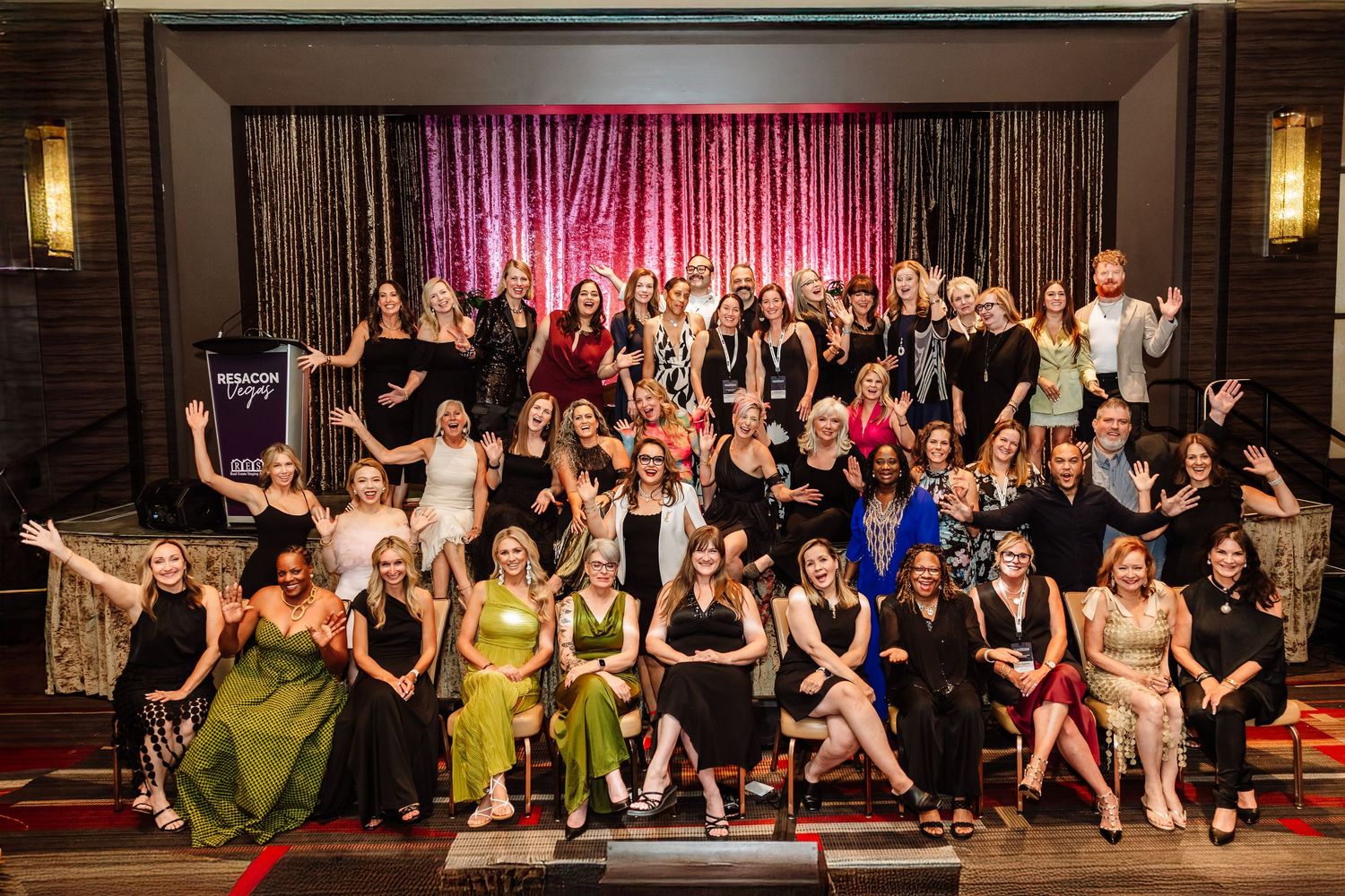 Large group of women posing together on stage at an awards gala event in elegant attire.