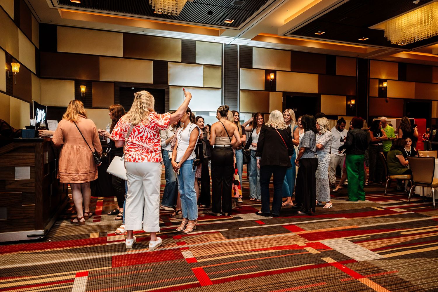 Diverse group of conference attendees networking in a large hotel ballroom event space.