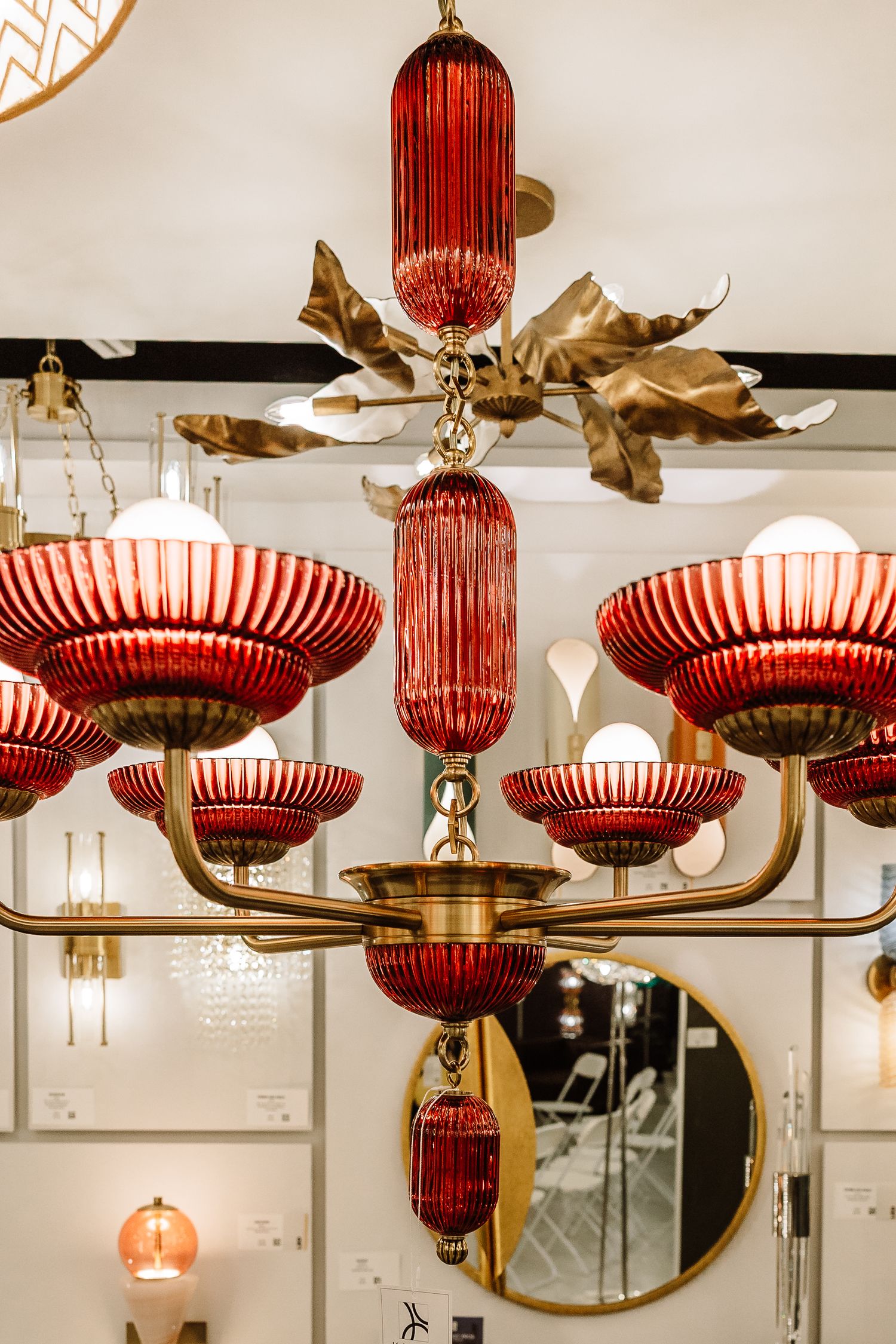 A stunning red and brass chandelier with ribbed glass shades displayed in a lighting showroom.