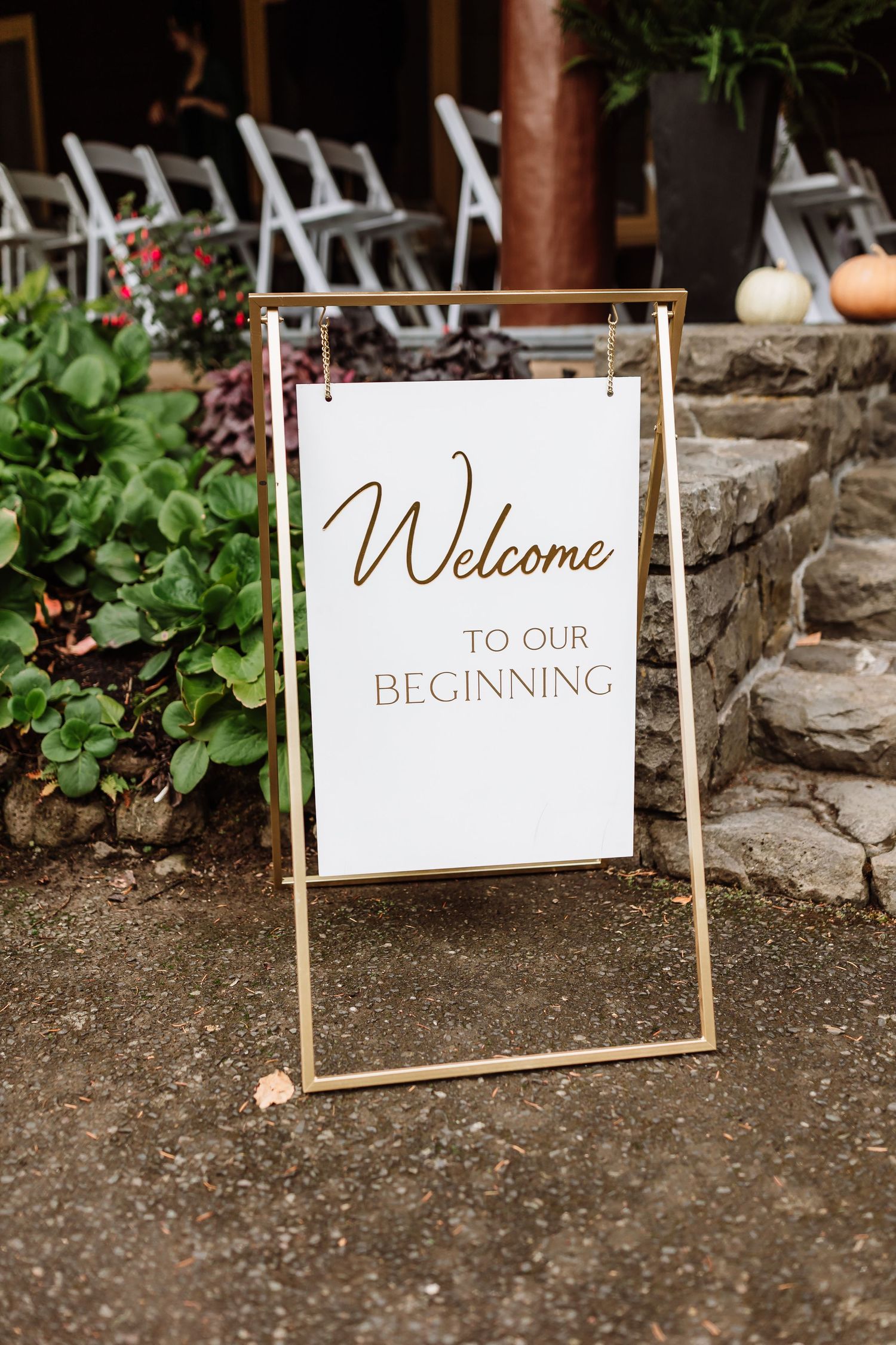 Gold-framed welcome sign reading Welcome to Our Beginning displayed at outdoor wedding ceremony.