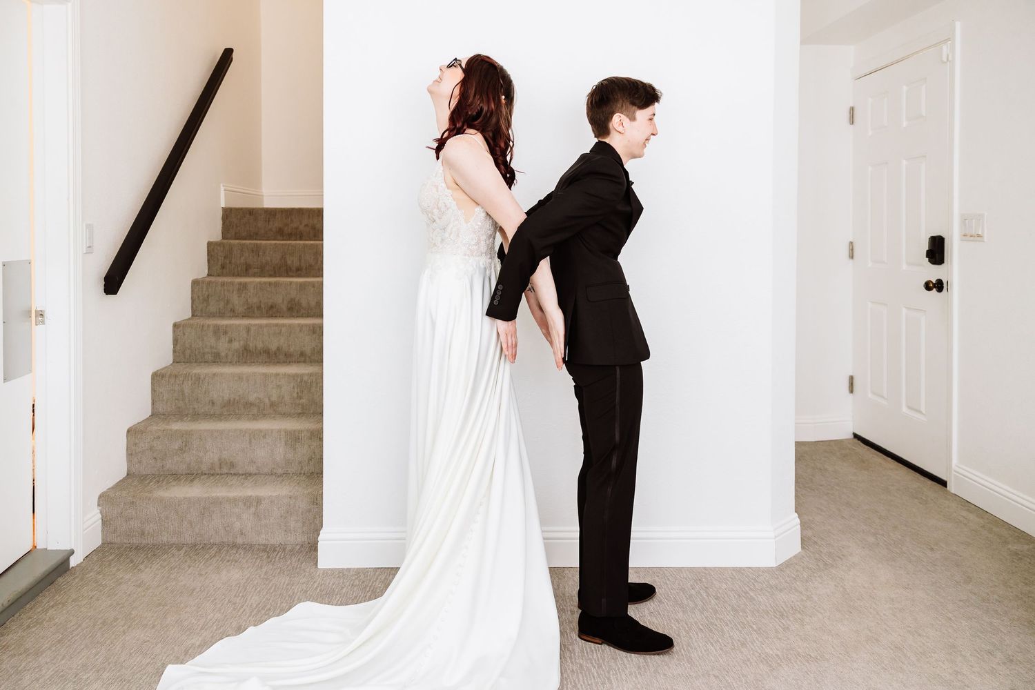 Bride and groom stand back-to-back in elegant wedding attire near a staircase for a first look moment.
