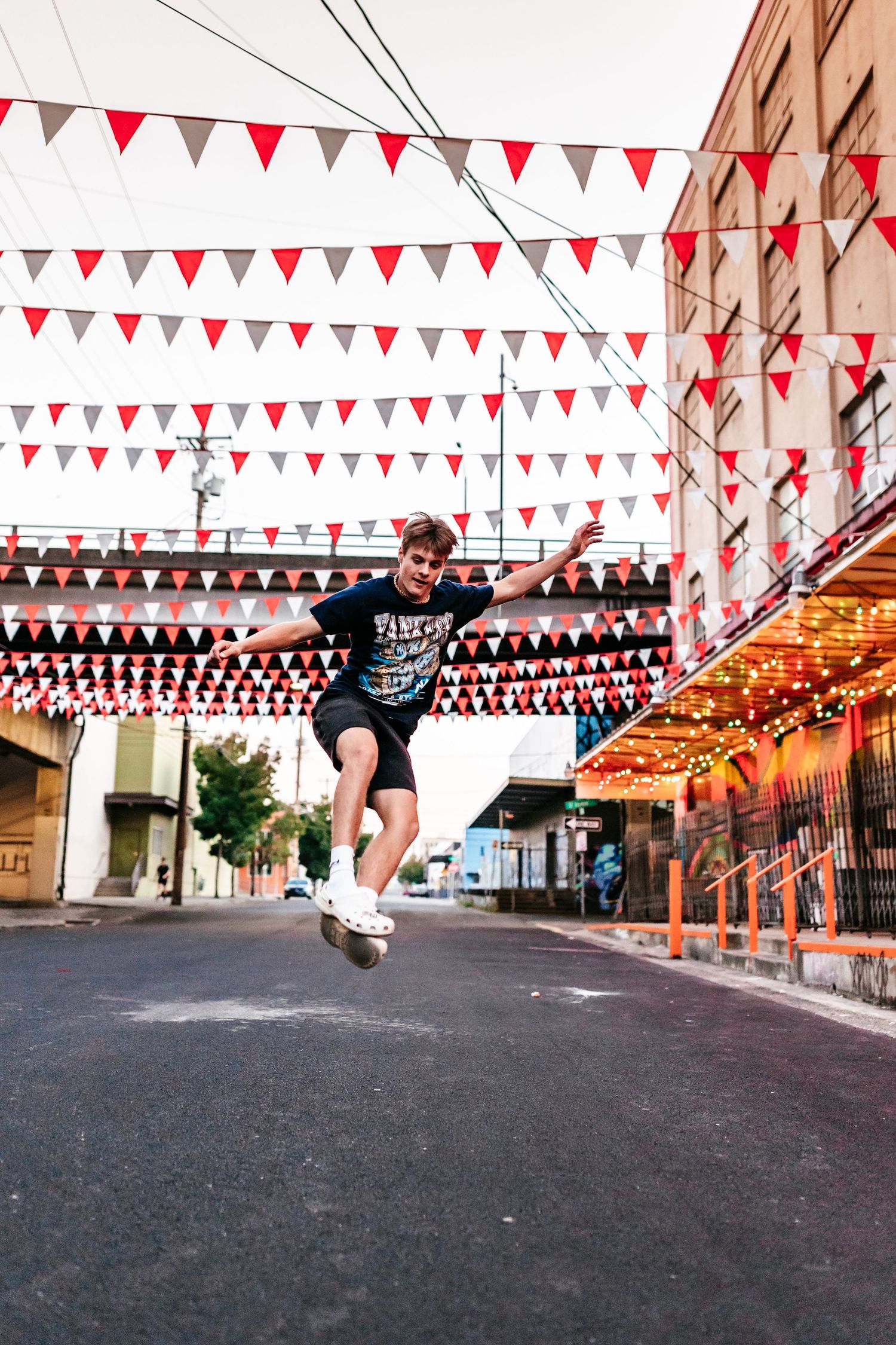 A young boy jumps joyfully in a street decorated with colorful red and white triangular bunting flags.
