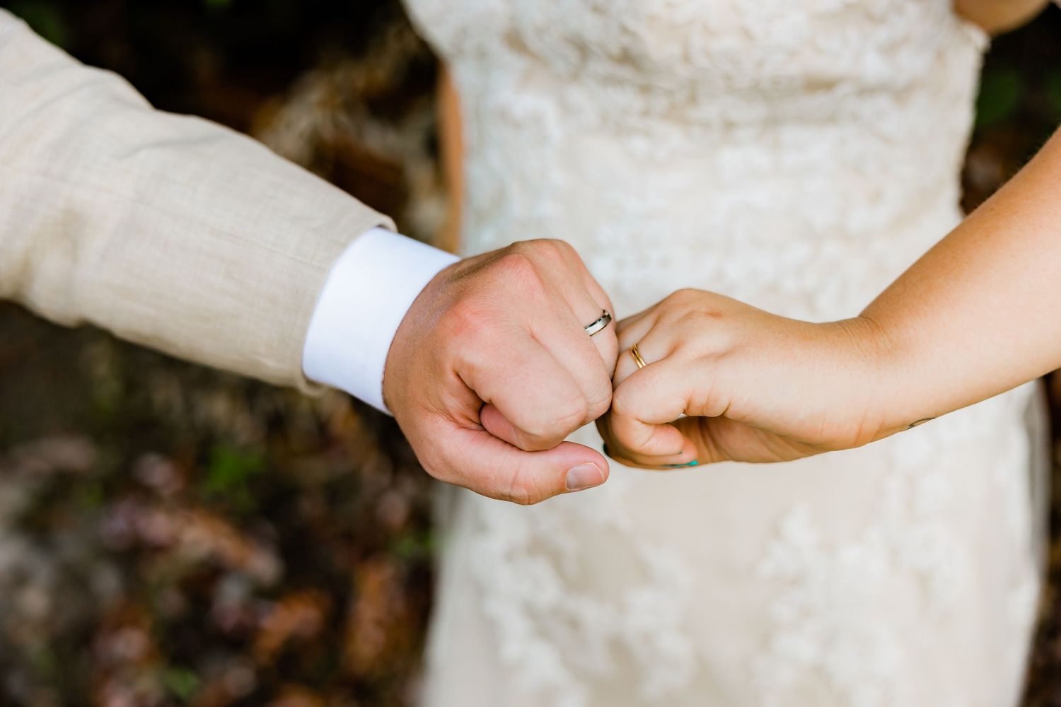 Close-up of newlyweds doing a pinky promise with wedding rings visible, wearing elegant wedding attire.