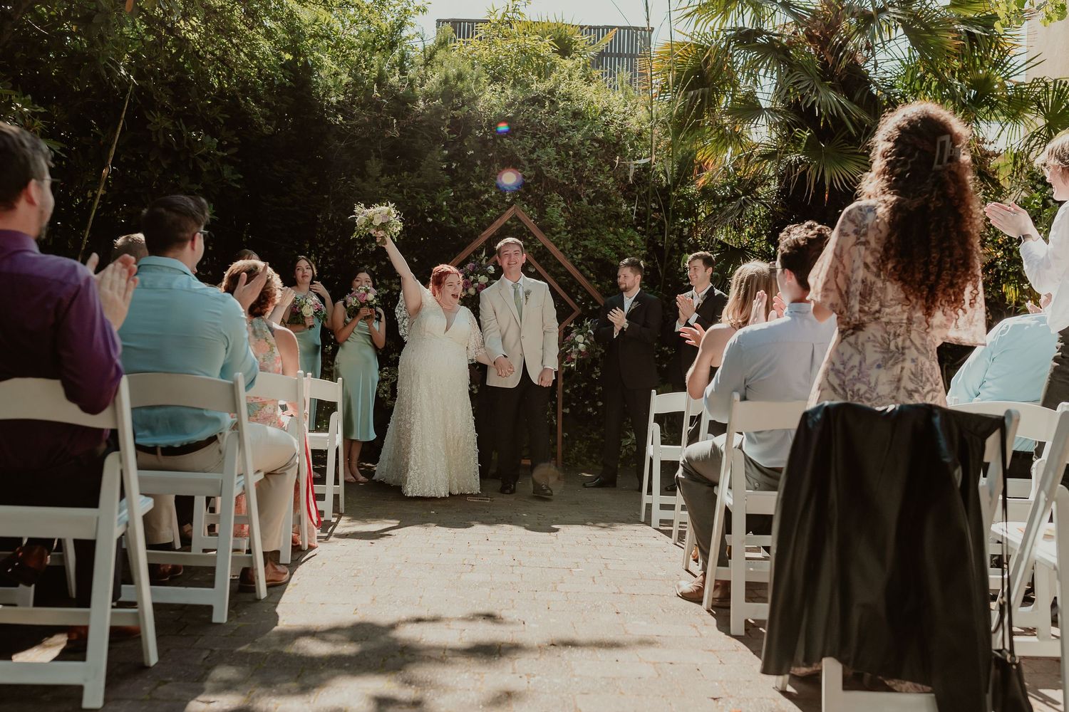Newlyweds walk back down the aisle after ceremony as guests cheer at outdoor garden wedding.