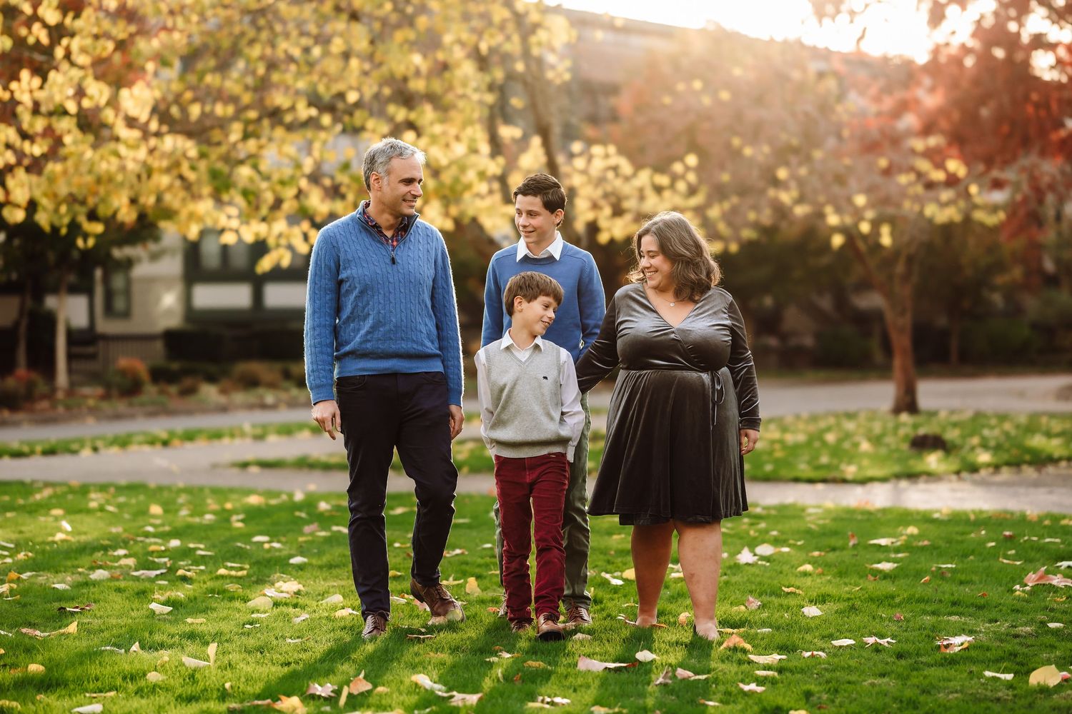Family of four walking together on green lawn surrounded by autumn foliage.