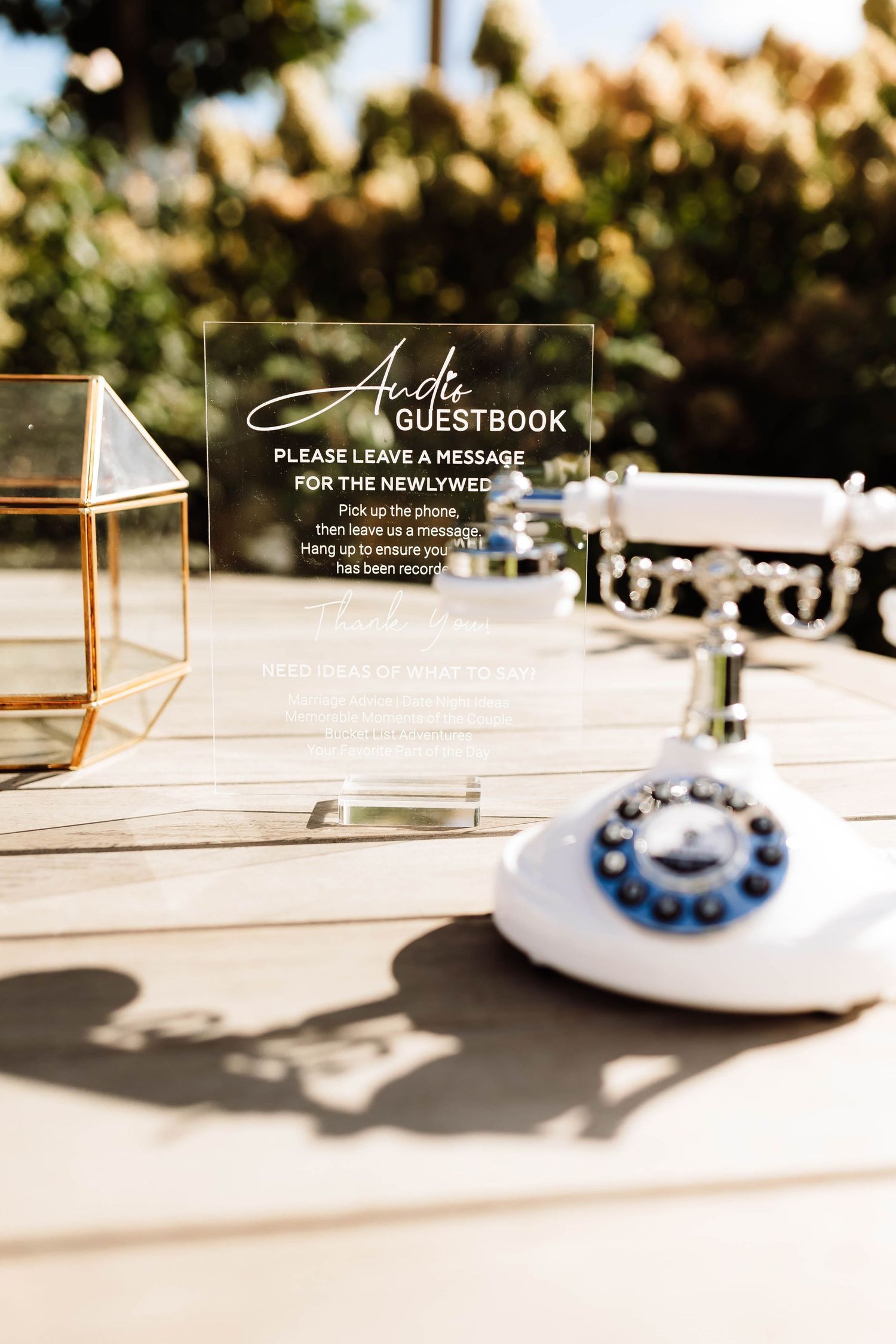 Audio guestbook station with vintage white rotary phone and acrylic sign asking guests to leave a message for the newlyweds.