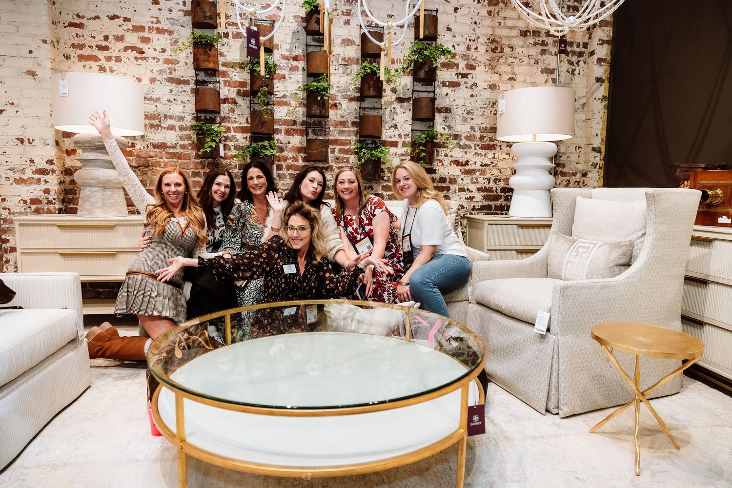 Group of nine smiling women posing together in an elegant furniture showroom.